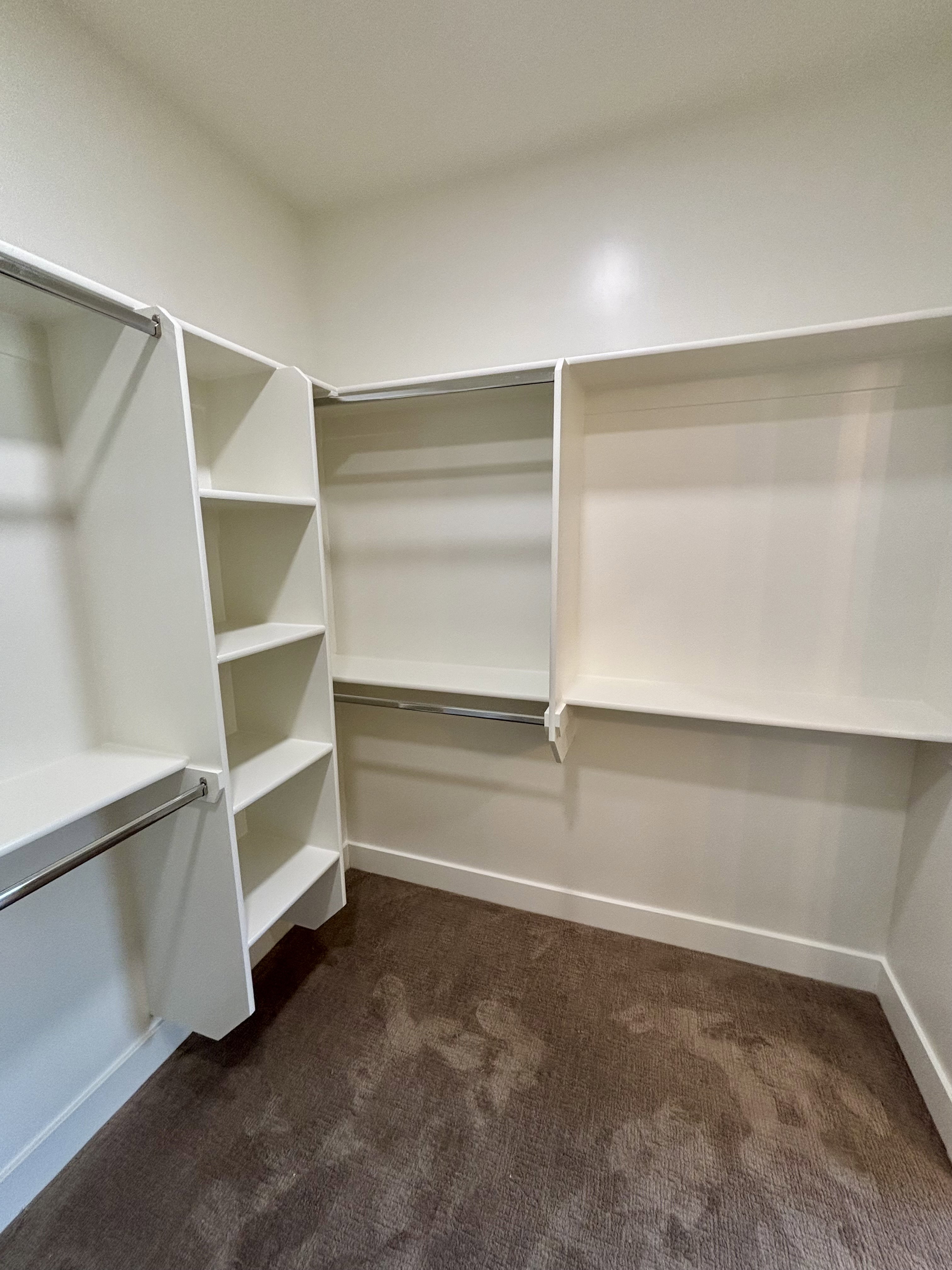 master walk-in closet featuring built-in white shelving, hanging rods, recessed lighting, a paneled door with a black knob, and carpet flooring