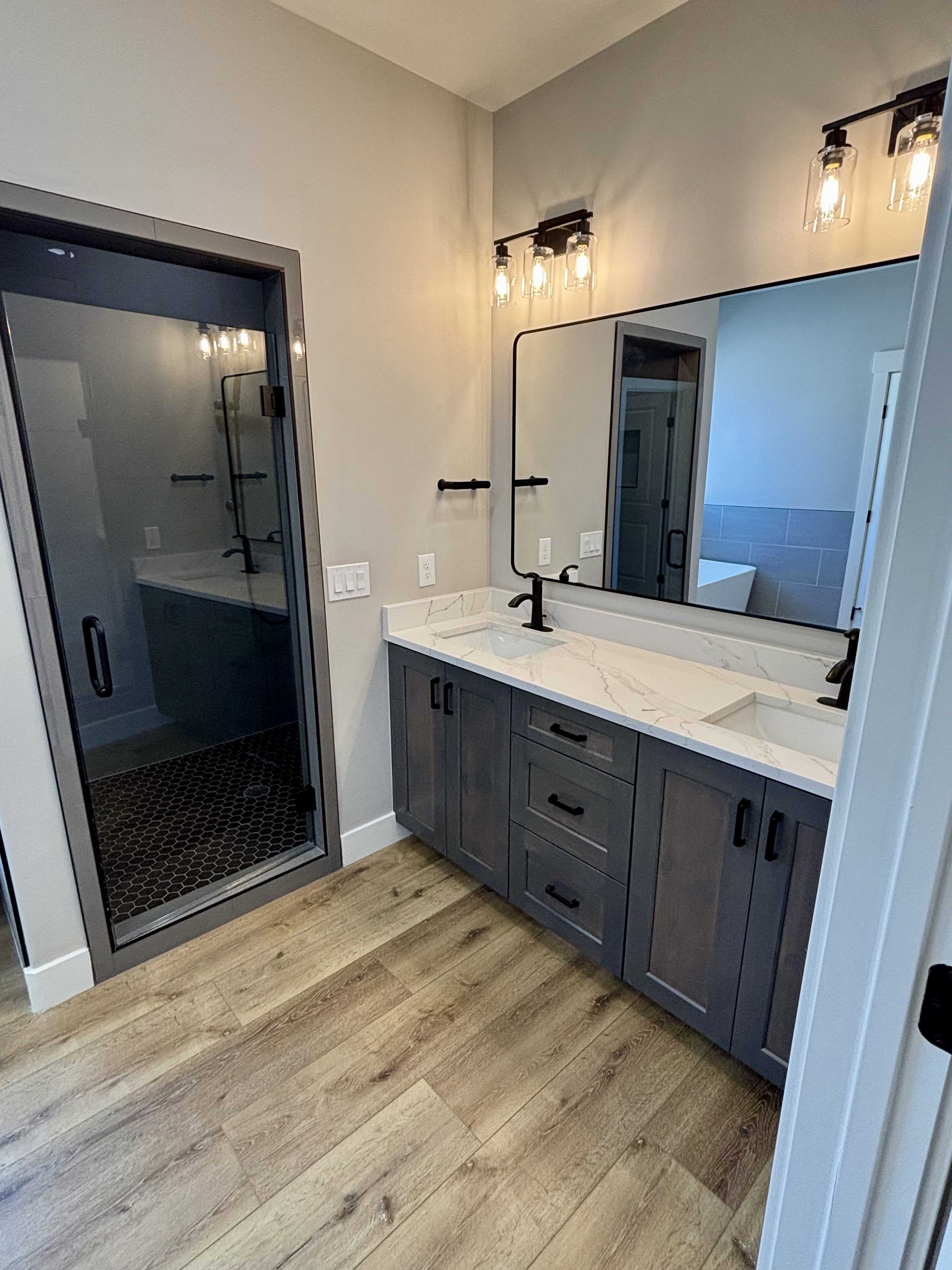 Master bath featuring a dual vanity with a white quartz countertop, matte black fixtures, walk-in shower with glass door