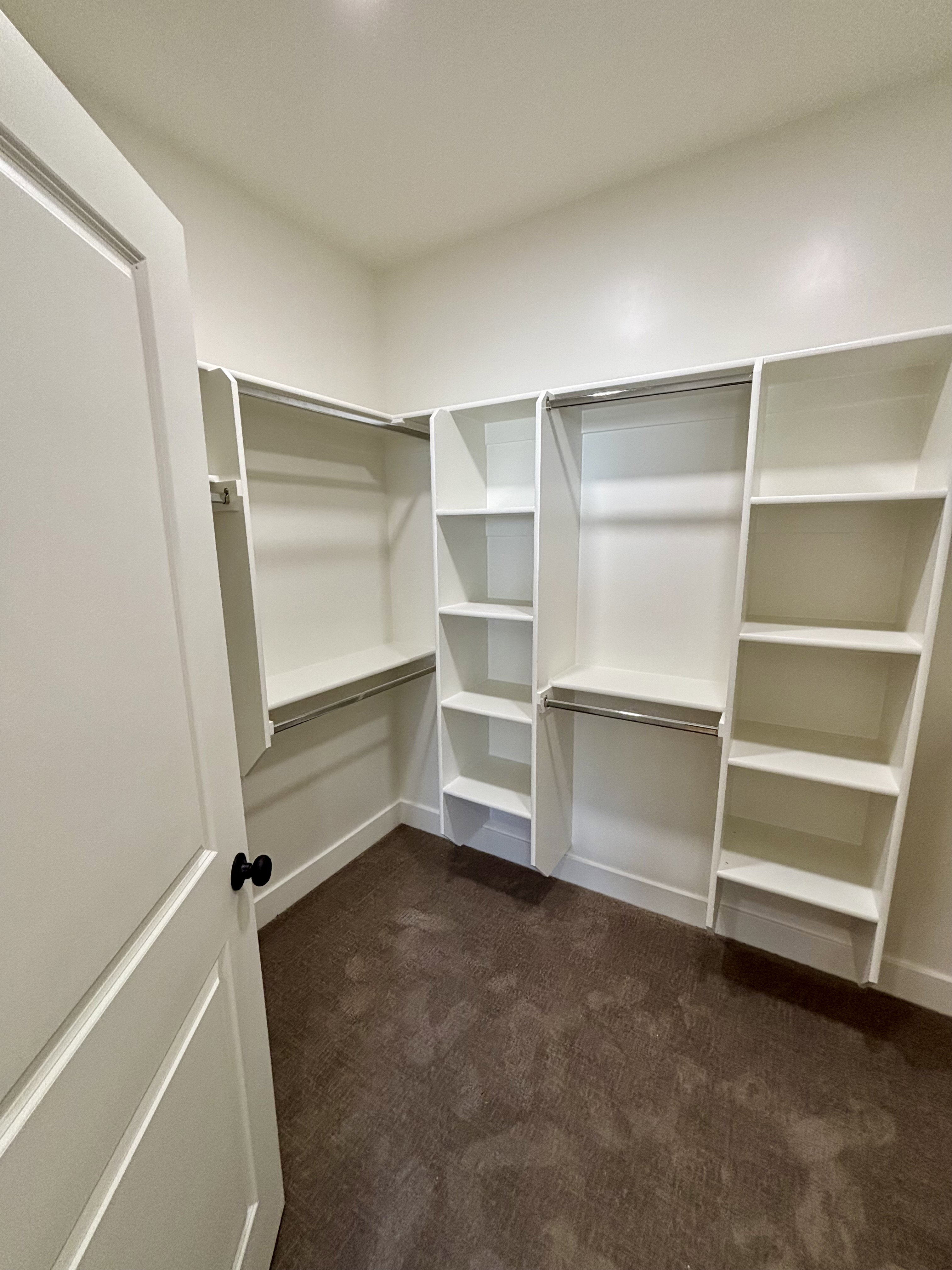master walk-in closet featuring built-in white shelving, hanging rods, recessed lighting, a paneled door with a black knob, and carpet flooring