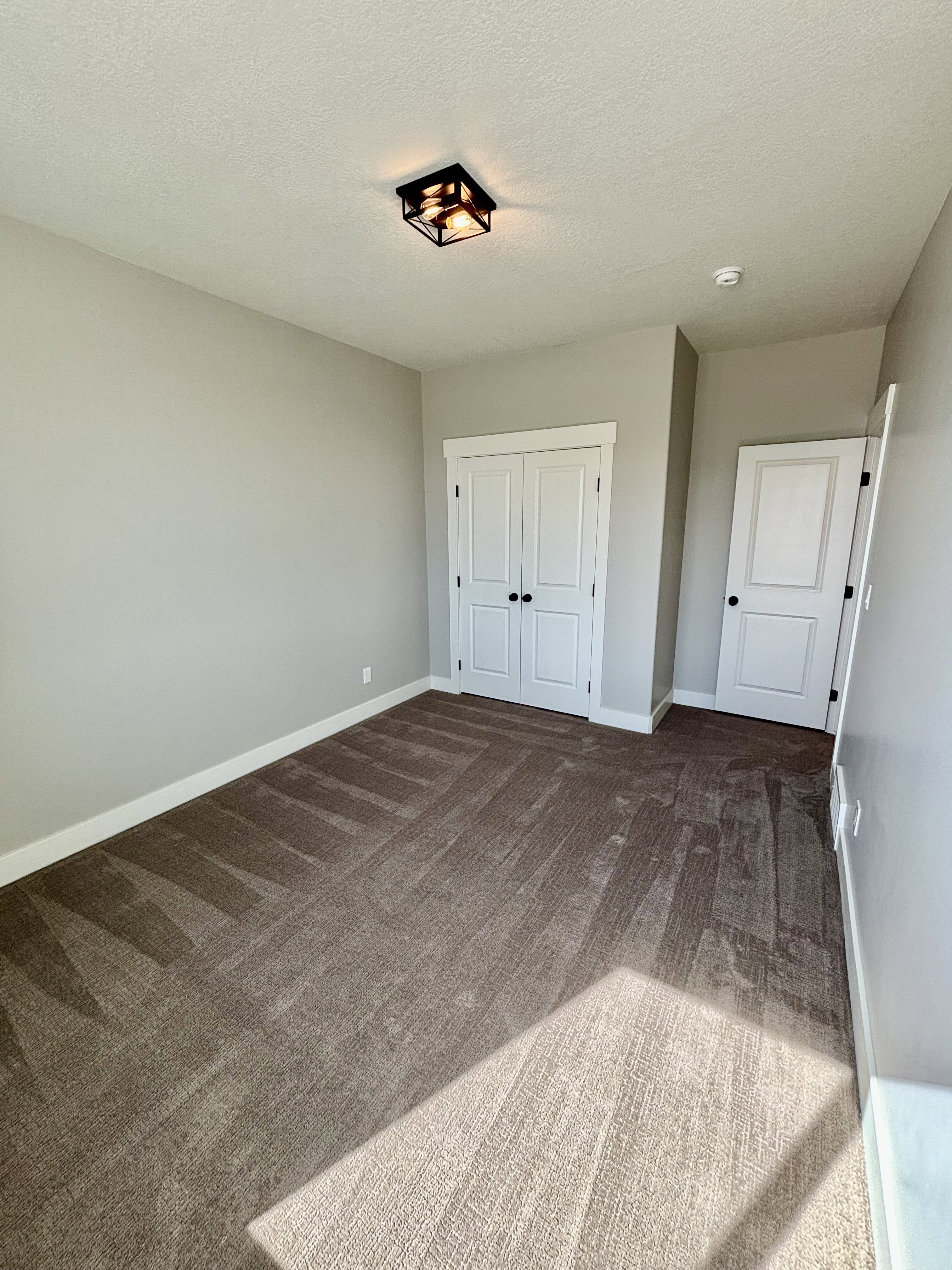 Light-filled room featuring a large window, neutral wall paint, patterned carpet flooring, and a contemporary ceiling light fixture