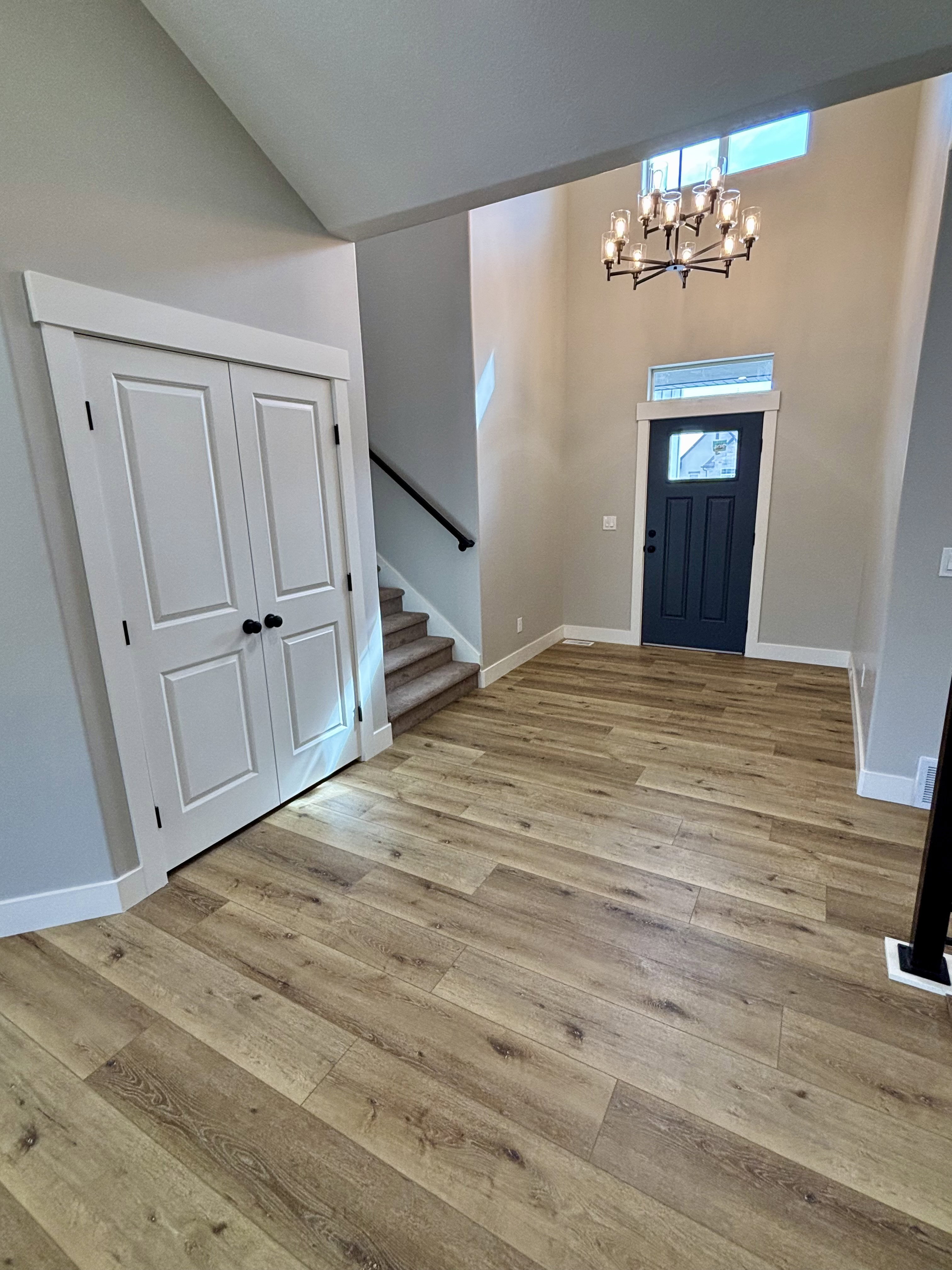 Entry foyer featuring wood-finish flooring, a dark blue-paneled door with transom window, a contemporary chandelier and coat closet