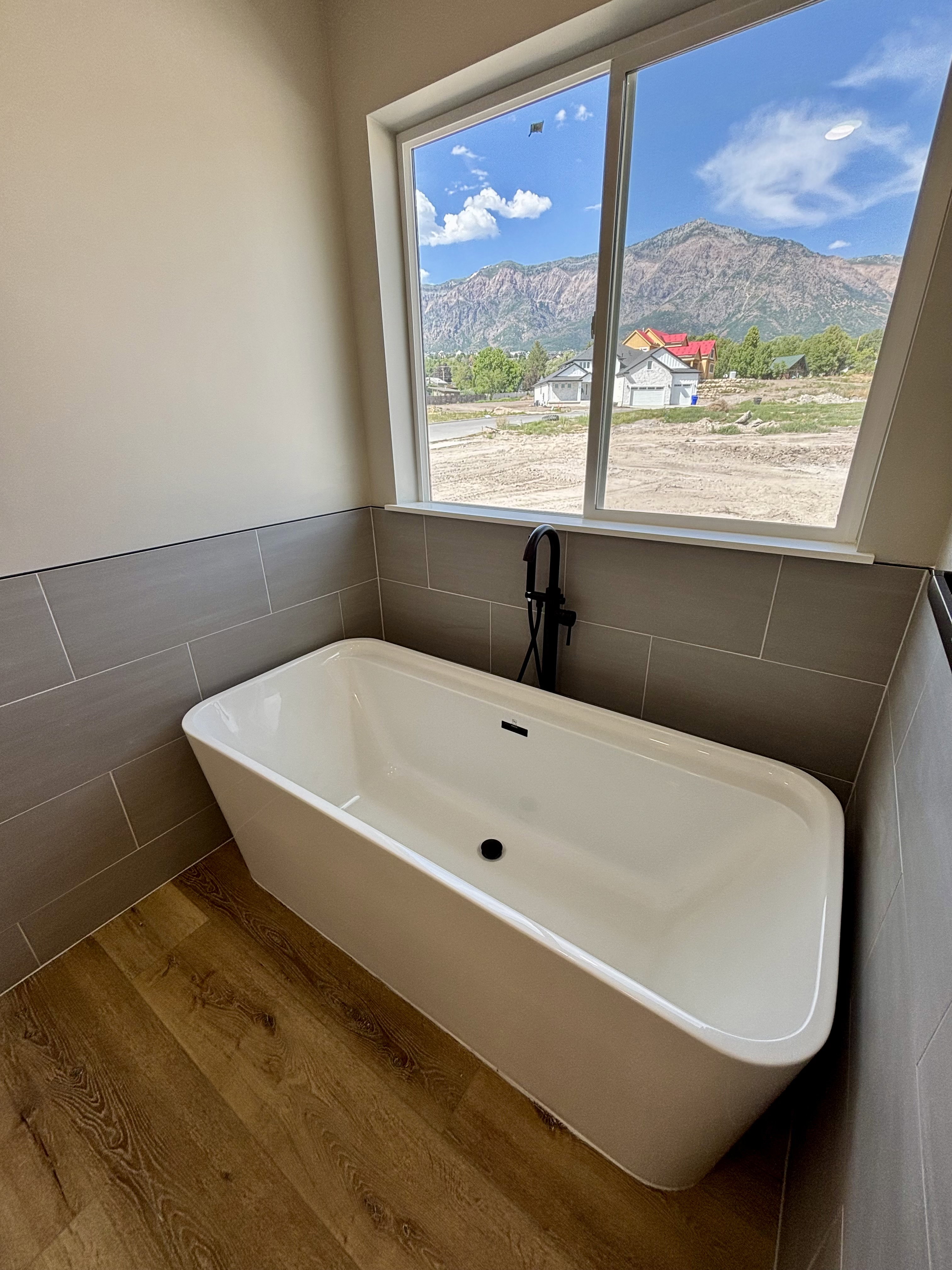 Freestanding soaking tub with a matte black floor-mounted faucet, set against a tiled accent wall and lvp wood style flooring