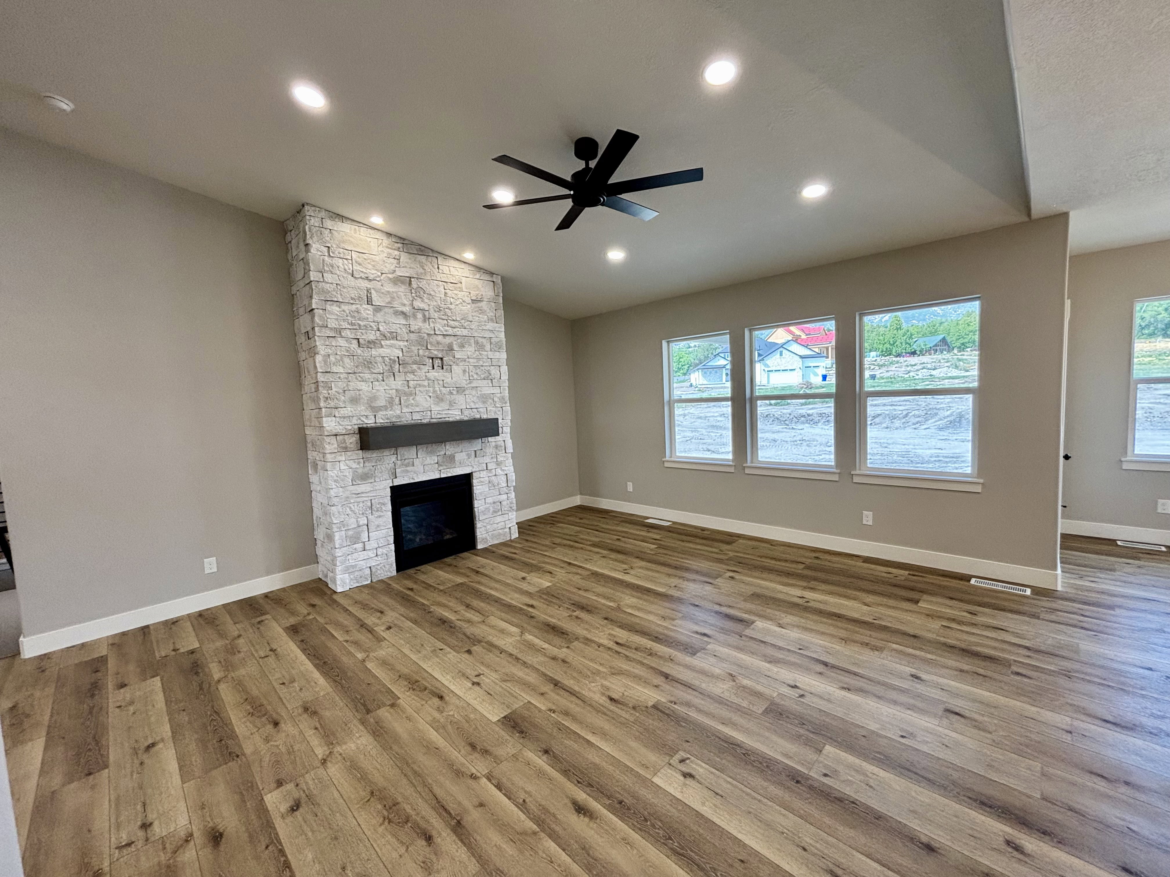 Spacious living area featuring a floor-to-ceiling stacked stone fireplace with a dark wood-finish mantel, lap style wood flooring, recessed lighting and a large ceiling fan