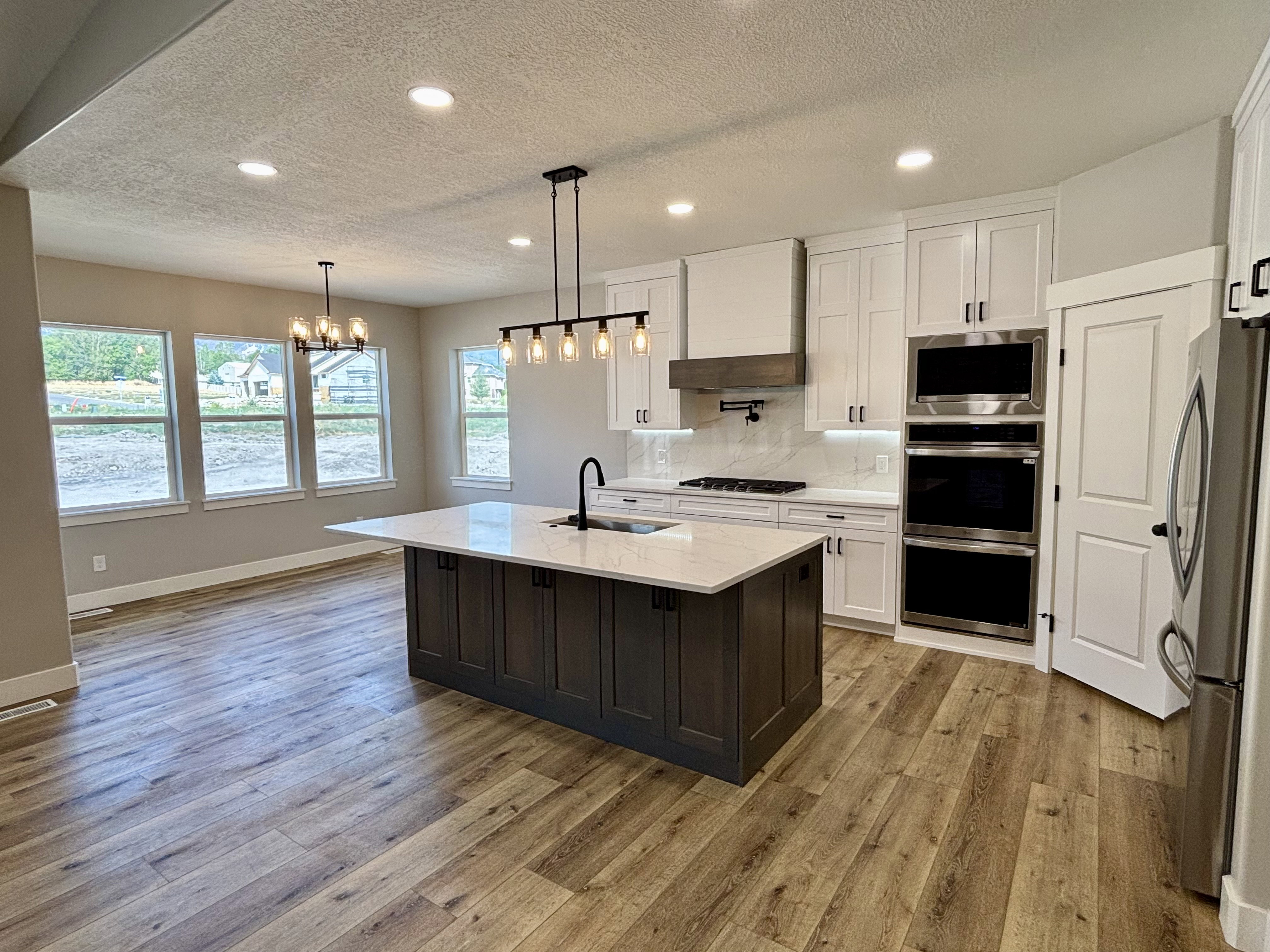 Kitchen featuring a central island with a light-toned quartz countertop, white cabinetry, integrated stainless steel appliances, lvp wood style  flooring, recessed lighting and dining/kitchen island lighting