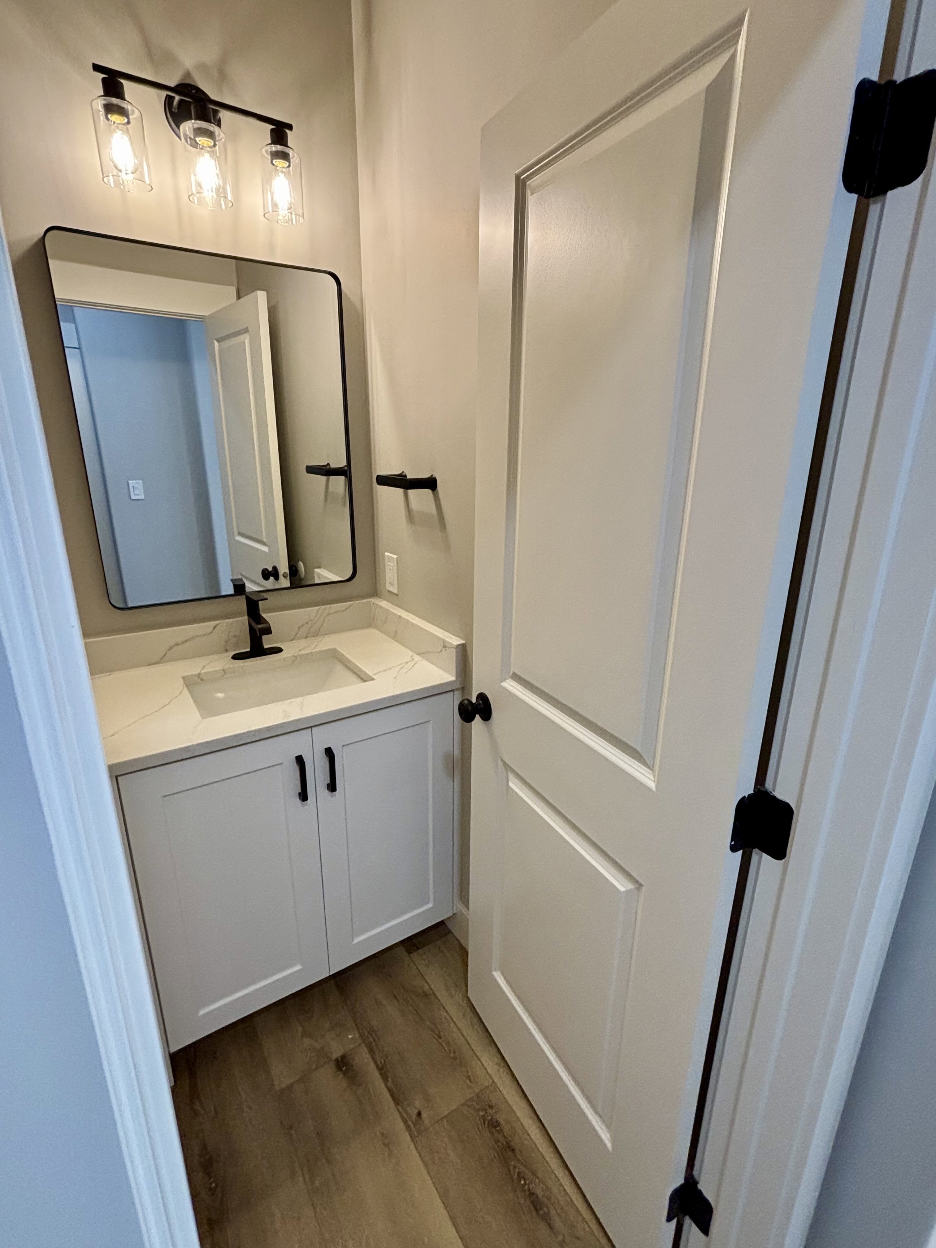 Contemporary bathroom featuring a white vanity with shaker-style cabinetry, a quartz countertop with an integrated sink, and lvp wood  style flooring
