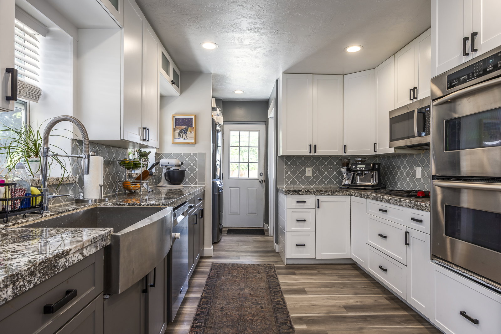 Modern kitchen with white upper and gray lower cabinetry, stainless steel appliances, and wood-finish flooring
