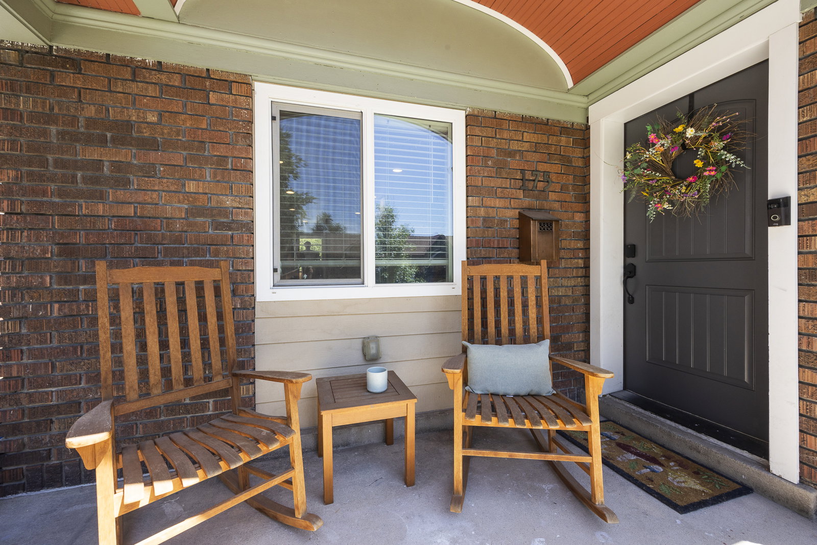 Covered front porch featuring brick and siding exterior, a dark-paneled entry door with white trim, and a window with blinds