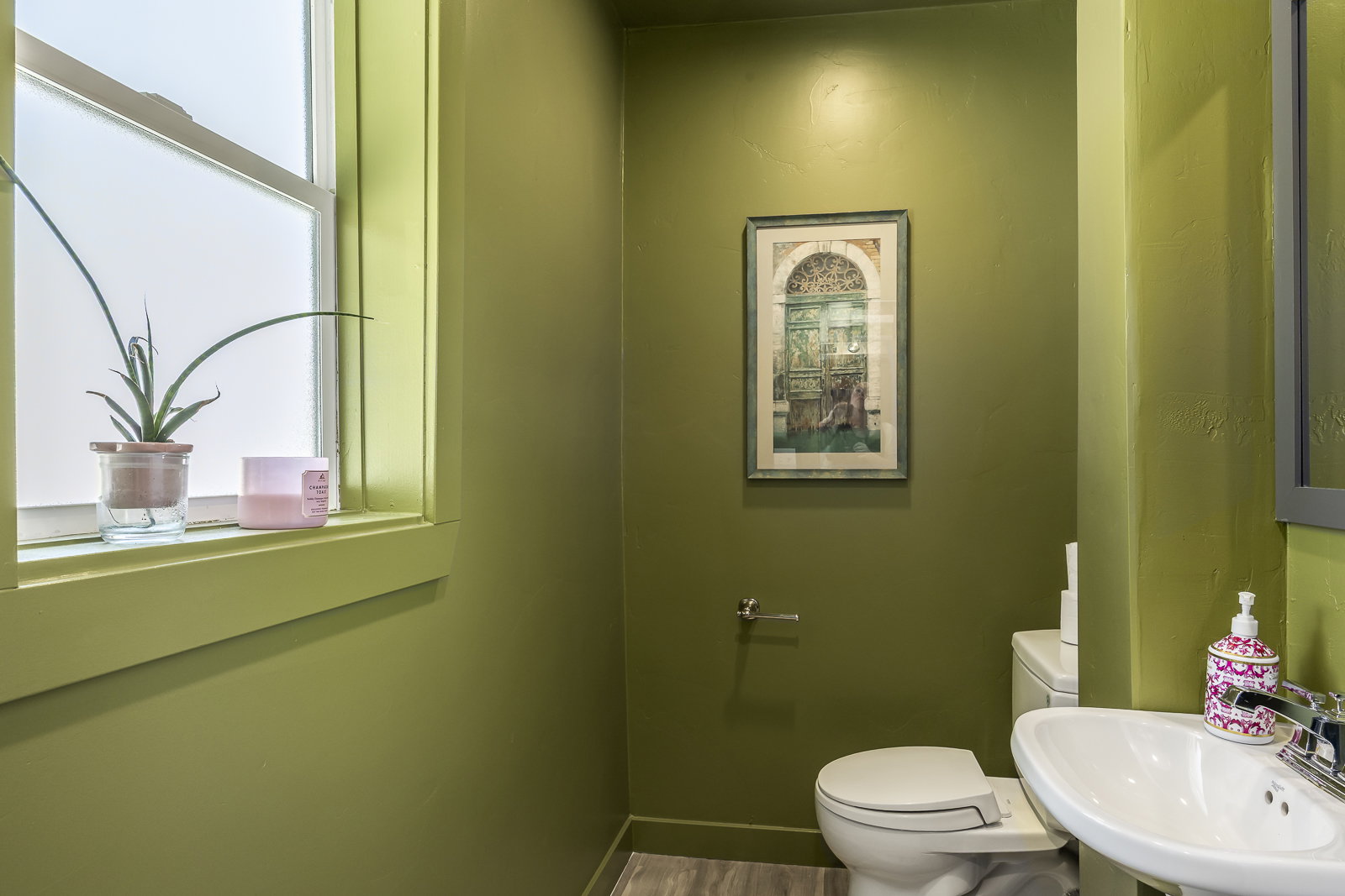 Compact bathroom featuring a pedestal sink, white toilet, and wood-finish flooring