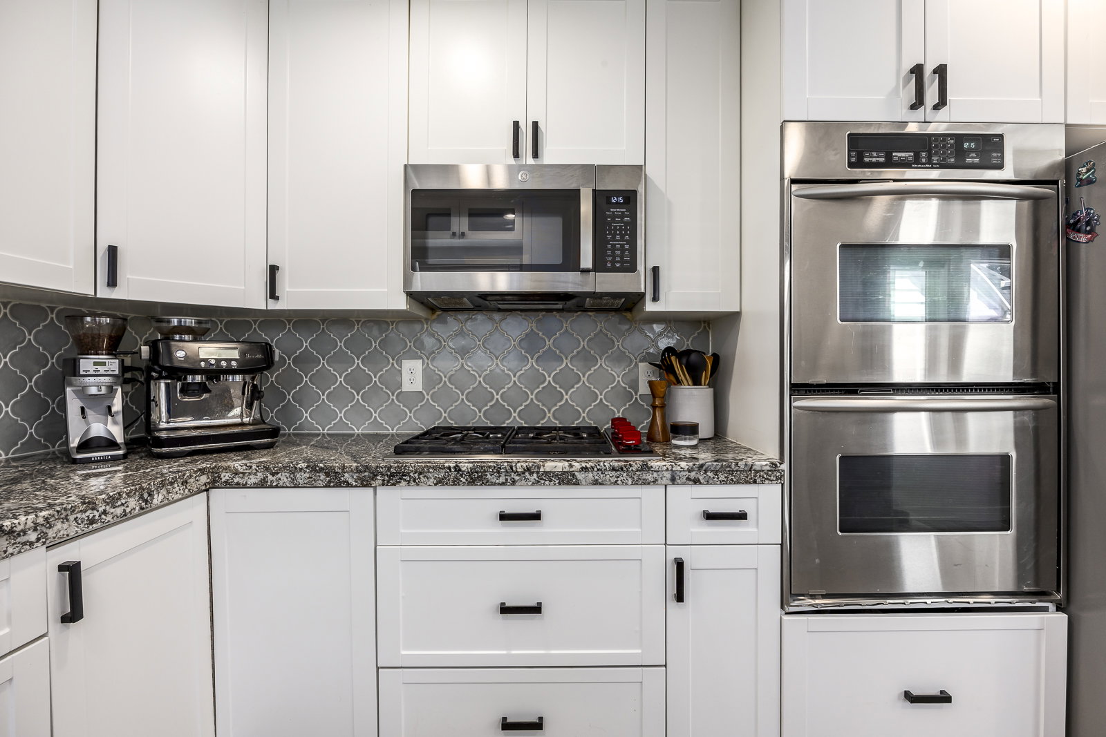 Kitchen featuring white cabinetry with matte black hardware, a grey arabesque tile backsplash, and speckled countertops