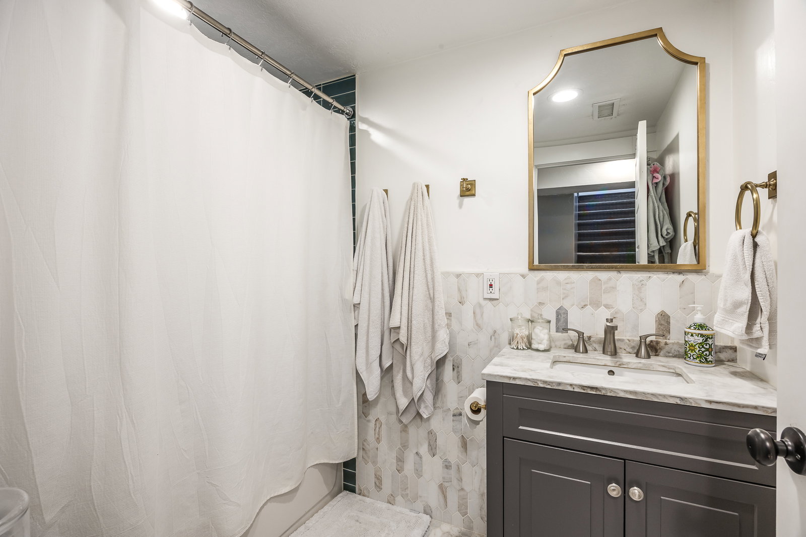 Bathroom featuring a vanity with a white countertop and dark gray cabinetry, a decorative framed mirror, and a tiled wall