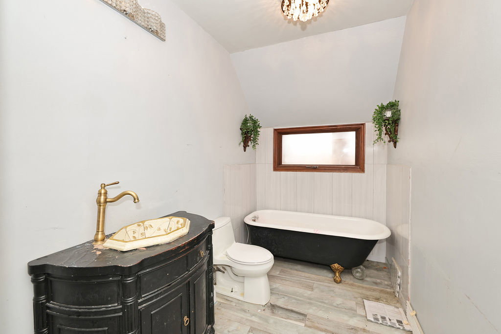 Bathroom featuring a vintage-style freestanding clawfoot tub, a wood-frame window, and a dark wood vanity with a brass-finish faucet
