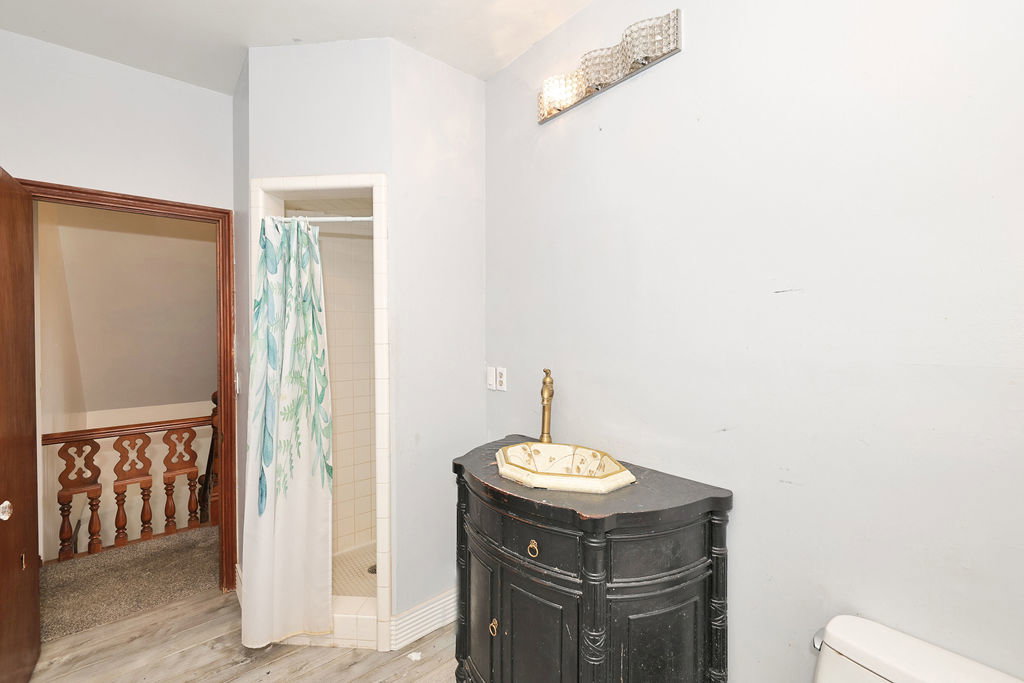 Bathroom featuring a curved black vanity with a decorative vessel sink, an ornate wall-mounted light fixture, and a tiled shower stall