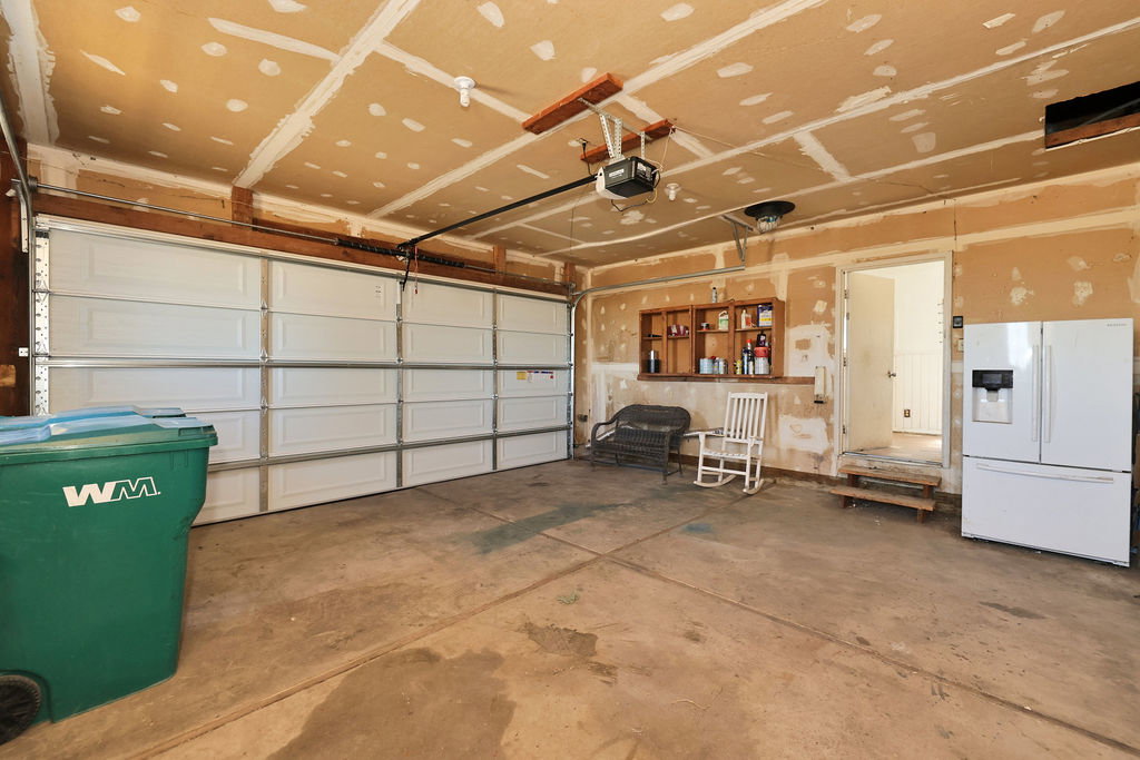 Spacious garage featuring a large overhead door, automatic opener, concrete flooring, built-in shelving, and direct entry