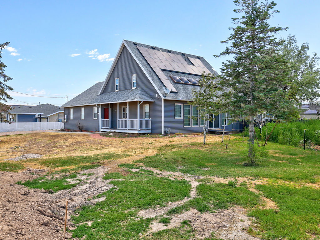 Gray two-story residence featuring solar panels, a covered front porch with white railings, and a contrasting red entry door
