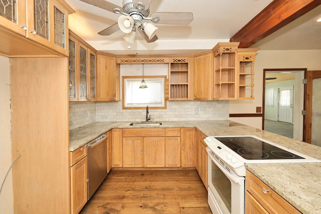 U-shaped kitchen featuring wood cabinetry, light-colored countertops, a tile backsplash, and wood-finish flooring