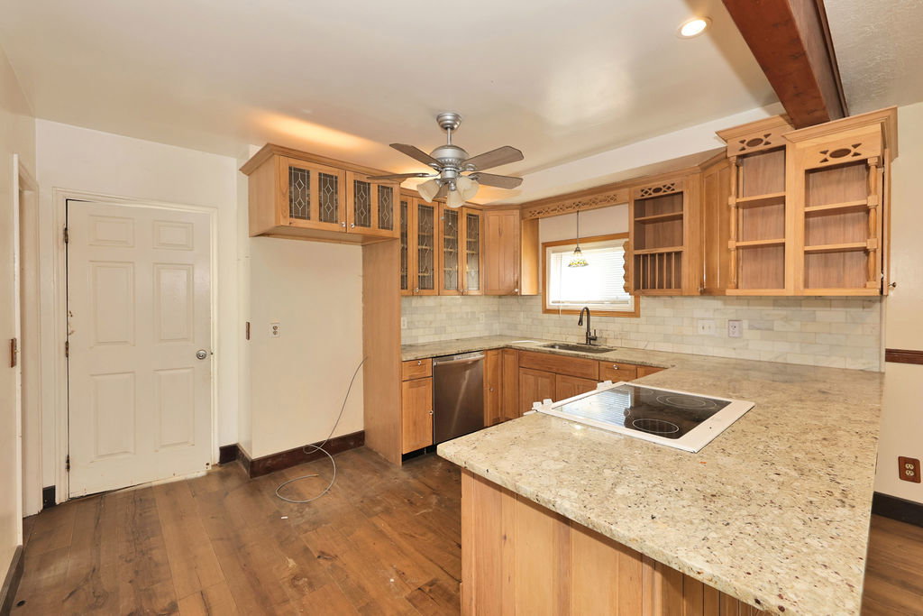 Kitchen featuring wood-finish flooring, light wood cabinetry with decorative glass inserts, and a textured tile backsplash