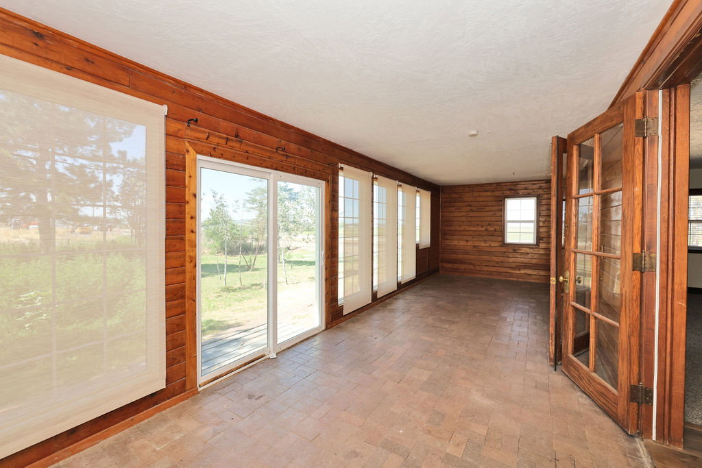 Spacious sunroom featuring extensive wood-finish wall paneling, a textured ceiling, and terracotta-style floor tiles