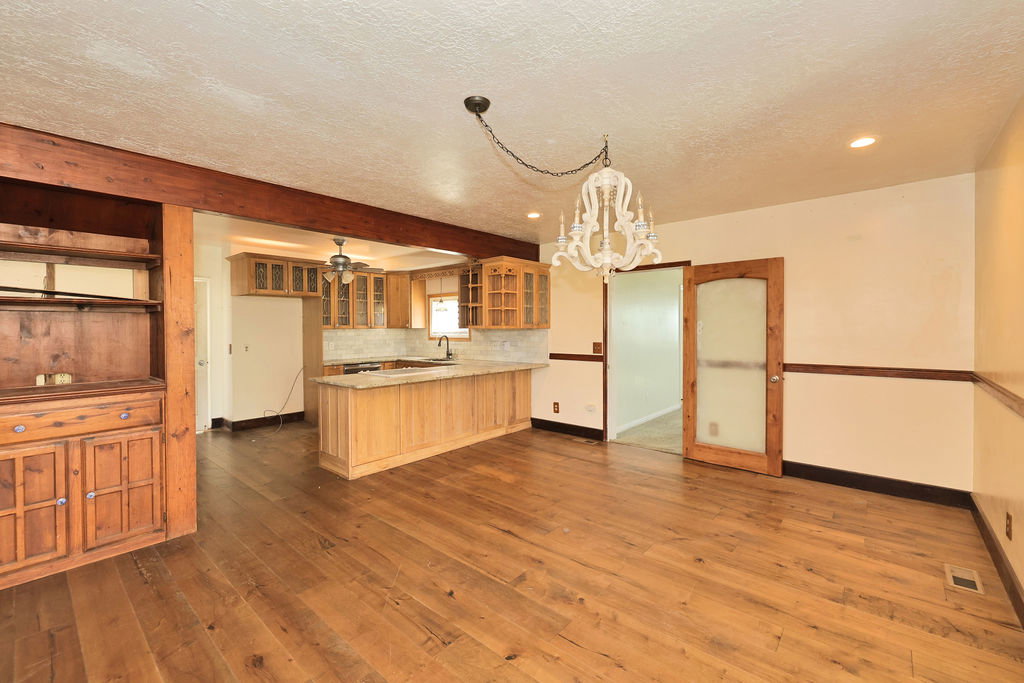Open-concept living area featuring wood-finish flooring, a built-in wooden hutch, a kitchen with light wood cabinetry, a breakfast bar, and a decorative chandelier