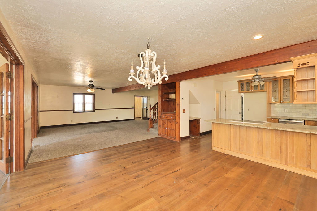 Expansive interior featuring wood-finish flooring, a decorative chandelier, exposed ceiling beams, and a kitchen island with a light-toned countertop