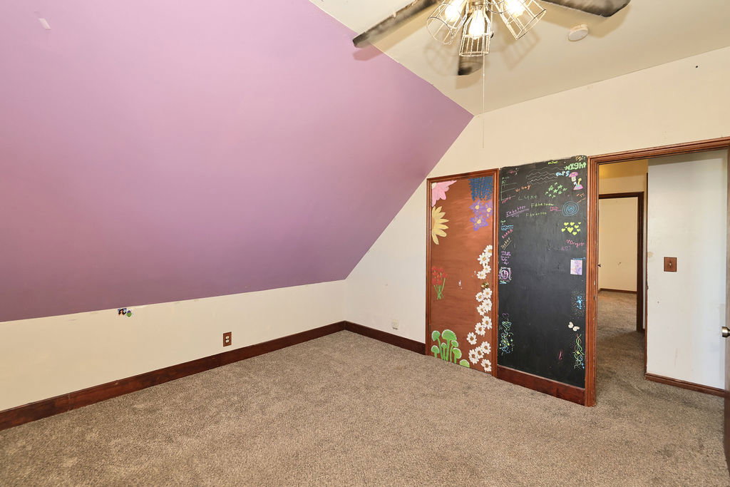 Carpeted room featuring a sloped ceiling, wood-finish baseboards, a ceiling fan with integrated lighting, and two sliding panel doors, one with a chalkboard finish