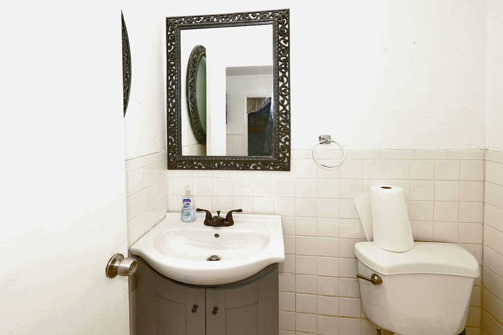 Bathroom featuring a pedestal sink with a gray vanity, white square-tiled wainscoting, and a decorative framed mirror