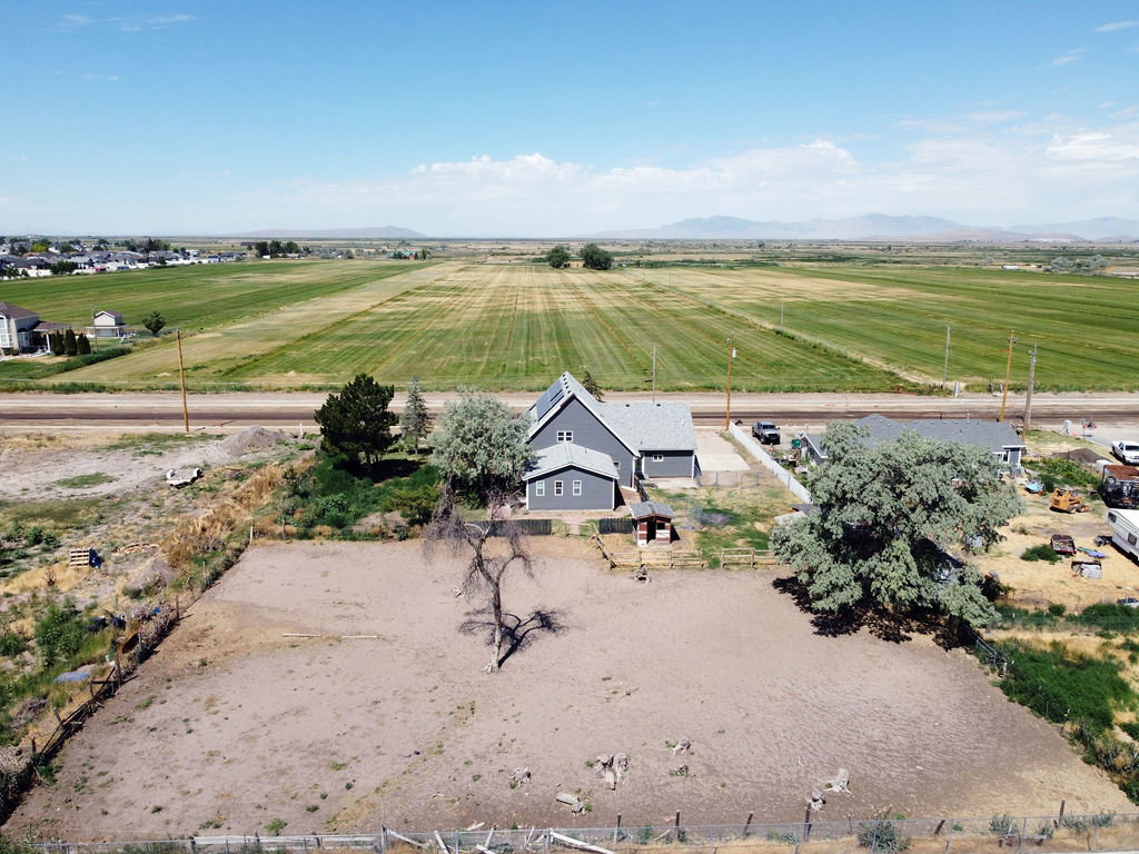 Spacious property featuring a grey residence with a shingled roof and solar panels, an additional detached building, and a fenced land area