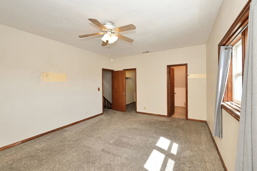 Carpeted room featuring a ceiling fan with integrated lighting, wood-trim windows, and multiple doorways providing access to other areas