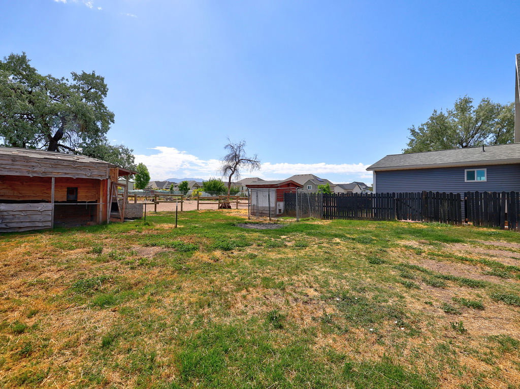 Expansive rear yard featuring an animal enclosure, a separate utility shed, a wood fence, and mature trees
