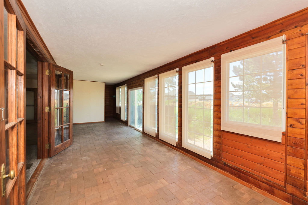 Sunroom featuring extensive natural wood paneling, multiple grid-pattern windows with roller shades, French doors with glass inserts, and brick-pattern tile flooring