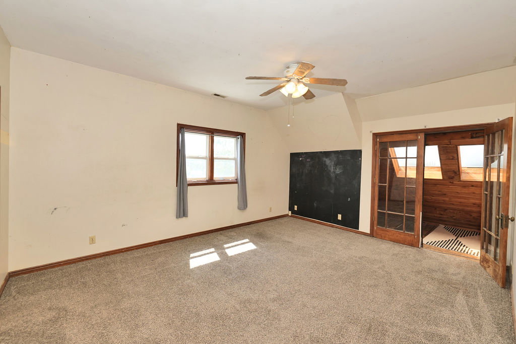 Carpeted room featuring a ceiling fan with integrated lighting, a double-hung window with wood trim, and a full wall of chalkboard surface