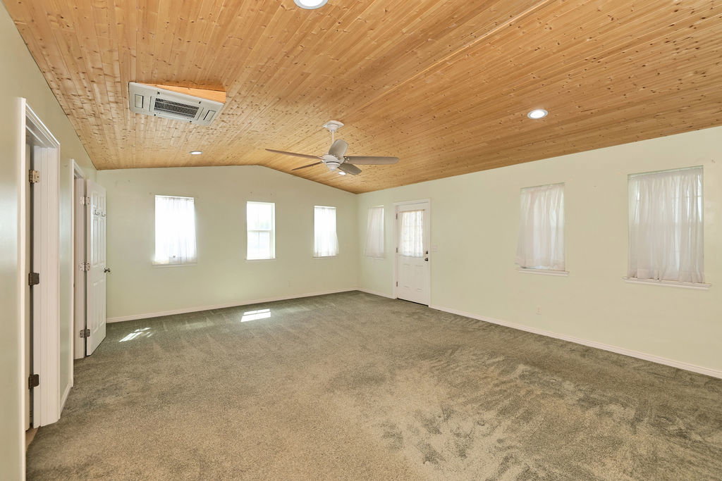 Spacious room featuring a vaulted wood-paneled ceiling with recessed lighting and a ceiling fan