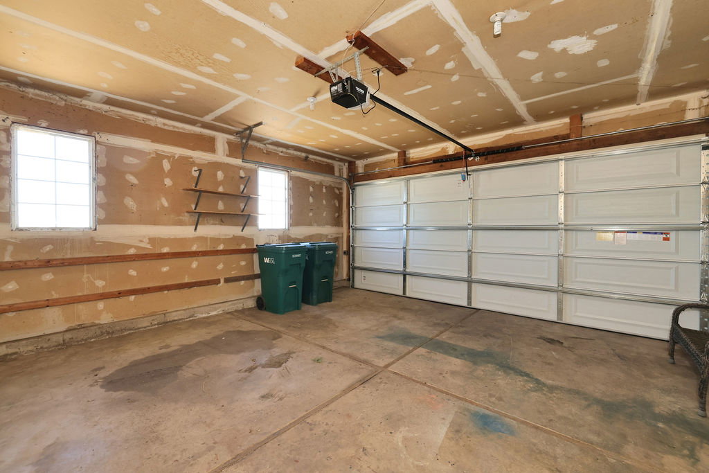 Spacious garage featuring a concrete floor, two windows providing natural light, a white paneled garage door, and a built-in shelving unit