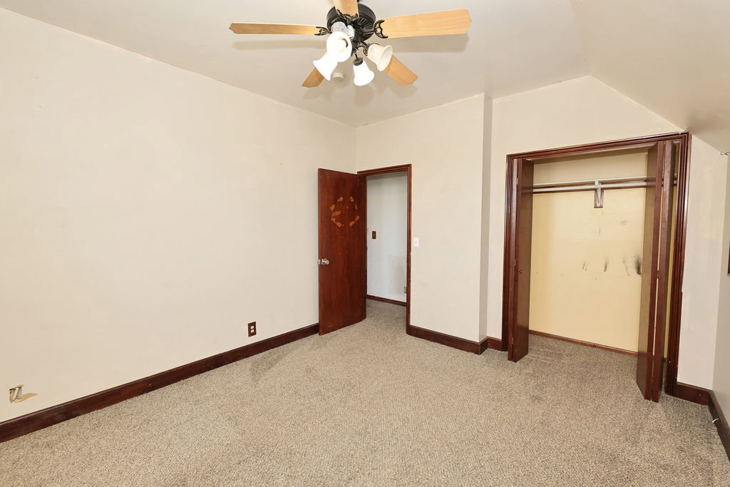 Carpeted interior room featuring a ceiling fan with integrated lighting, a wood-paneled door, and a closet with bifold doors and a clothing rod