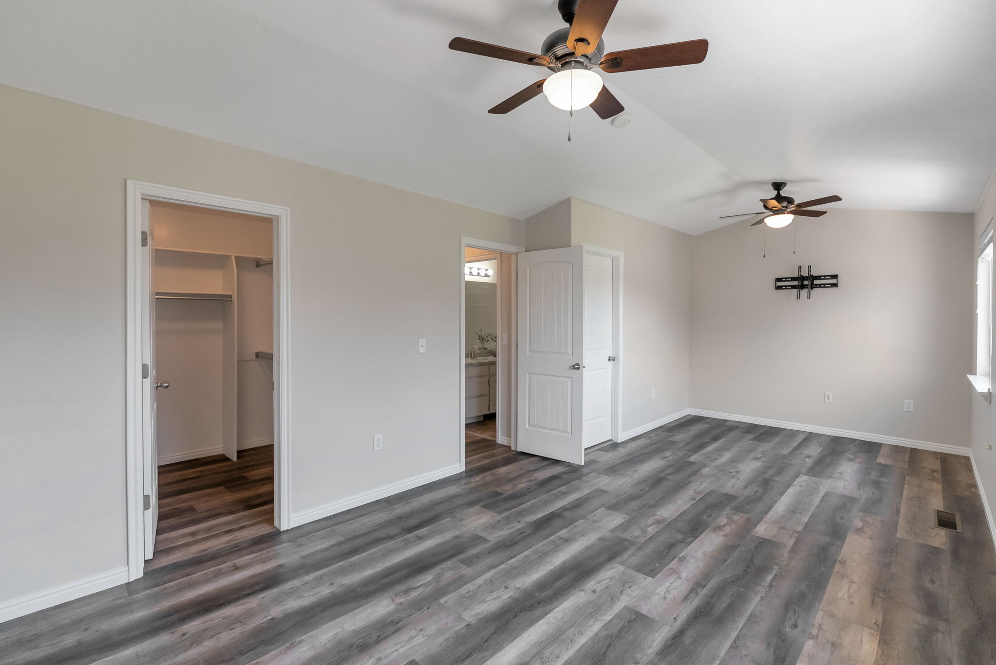 Spacious room featuring wood-finish flooring, light grey walls, and two ceiling fans with integrated lighting