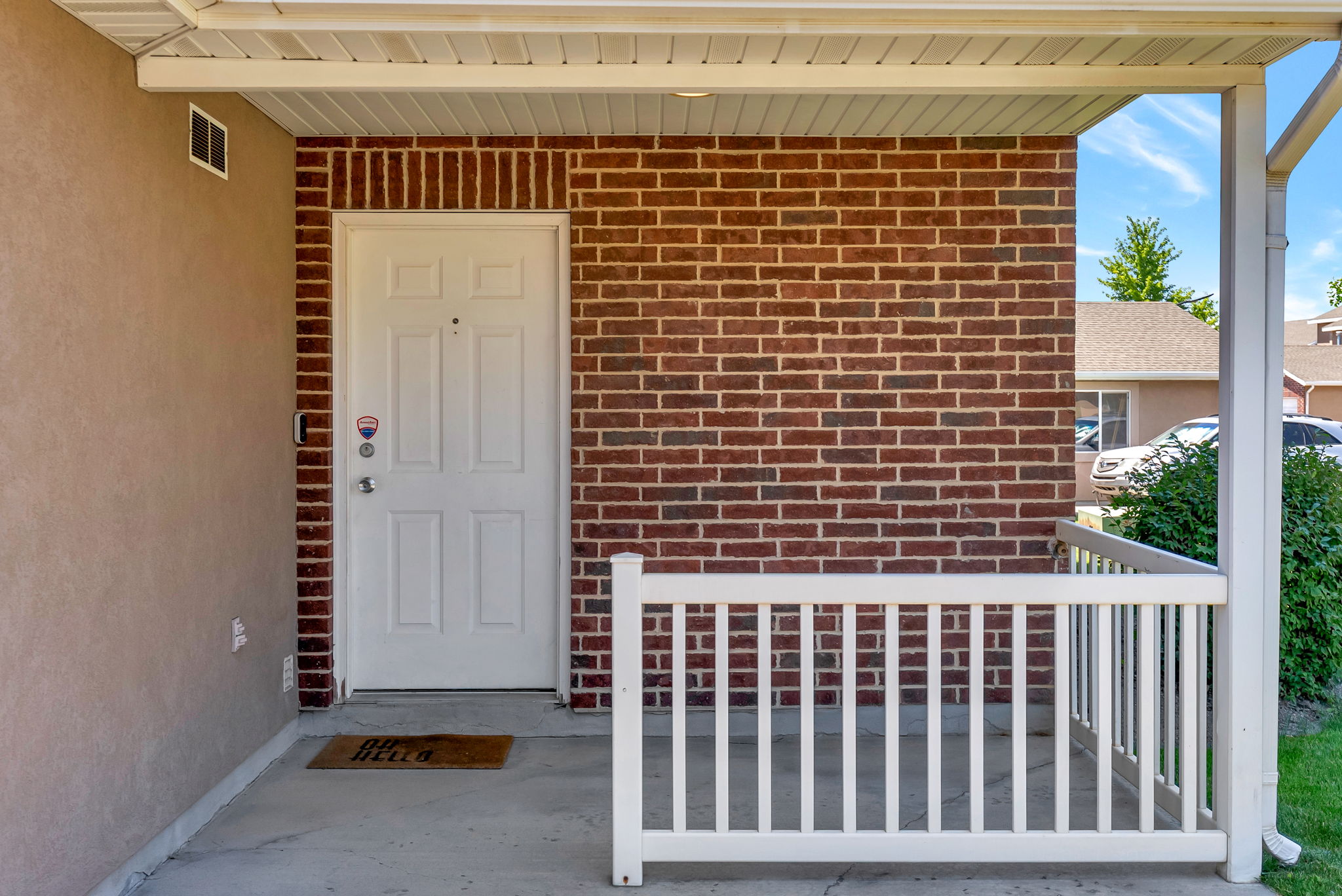 Covered porch entrance featuring a white panel door, brick facade, stucco siding, concrete flooring, and a white railing