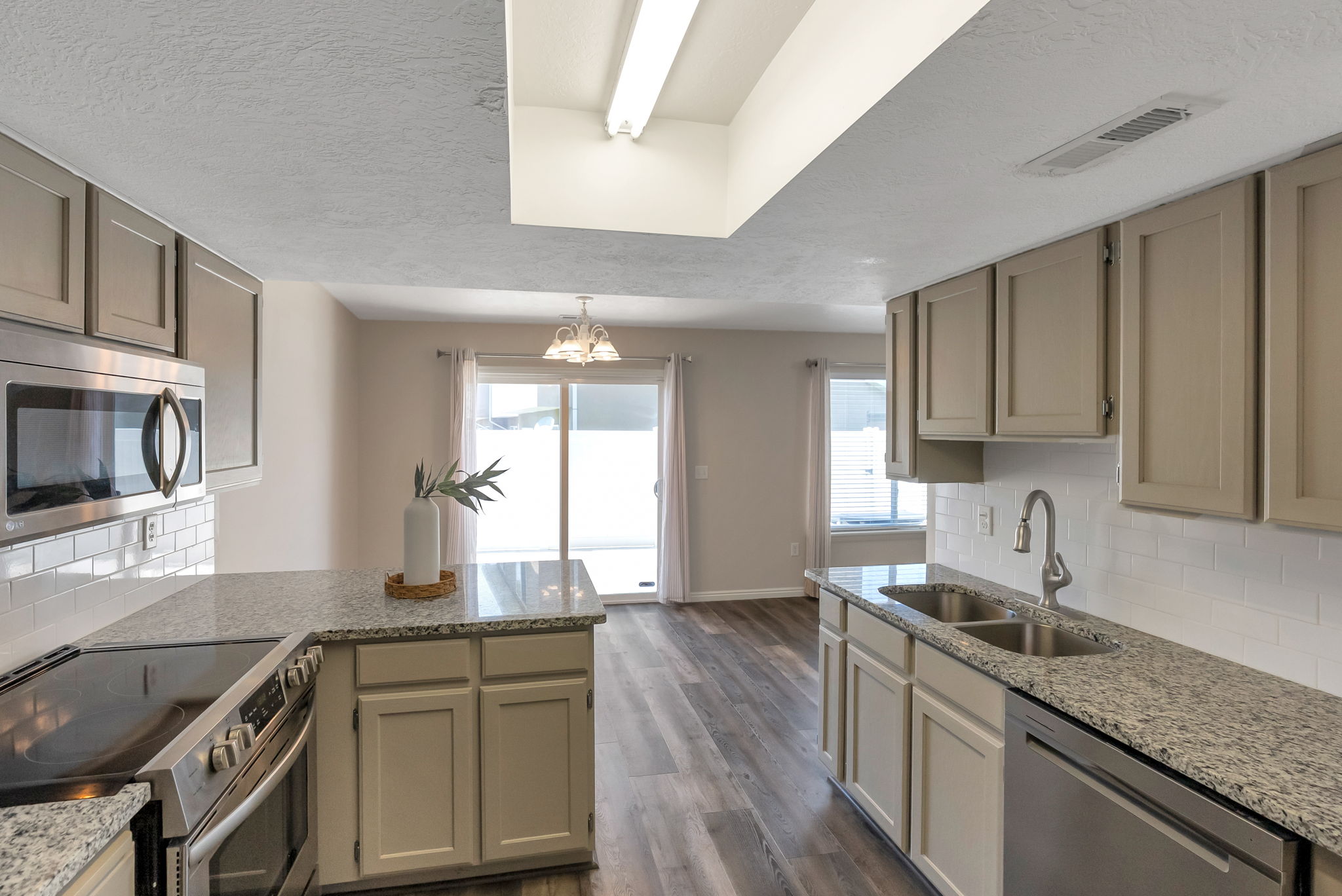 Kitchen featuring light-toned cabinetry, granite-style countertops, stainless steel appliances, a white subway tile backsplash, and wood-finish flooring