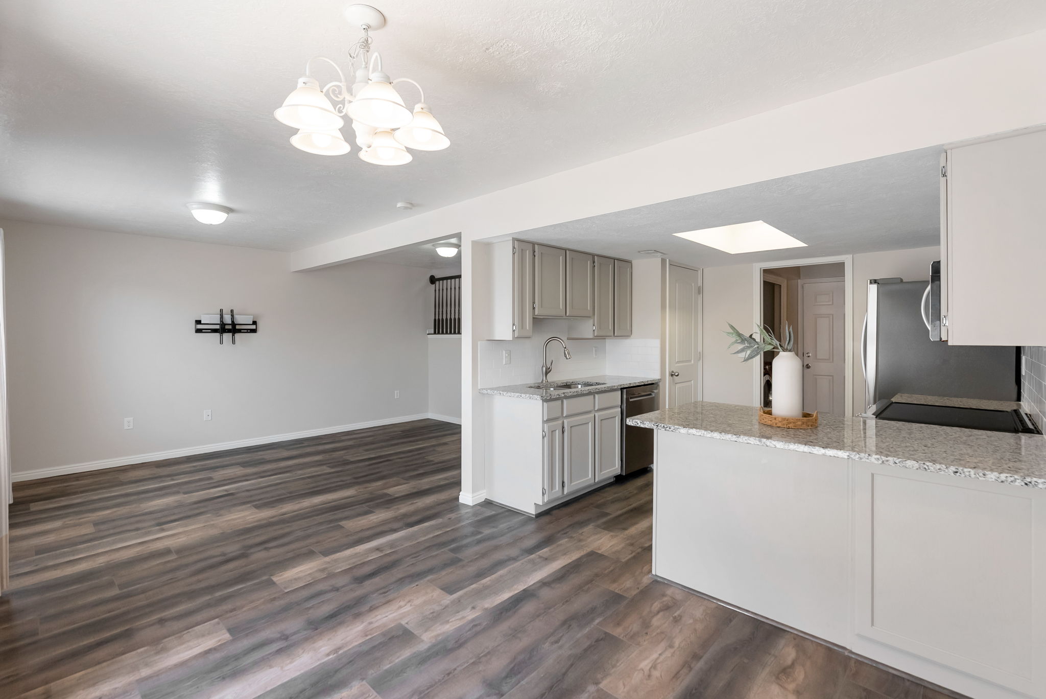 Open-concept living space featuring wood-finish flooring, a contemporary kitchen with light-colored cabinetry, a granite-style countertop, and a stainless steel appliance suite