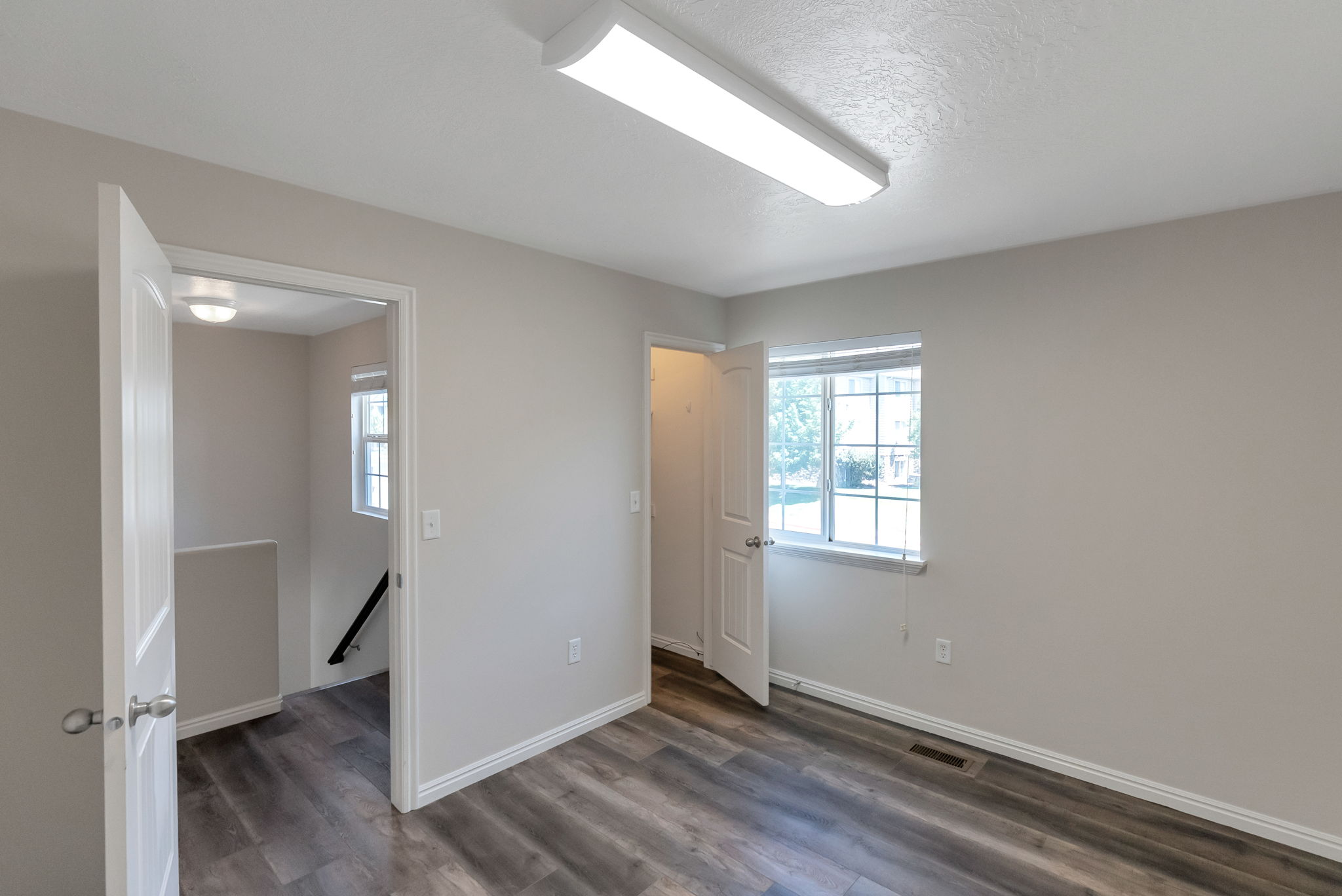 Spacious room featuring wood-finish flooring, light-toned walls, a double-hung window, and a flush-mount ceiling light