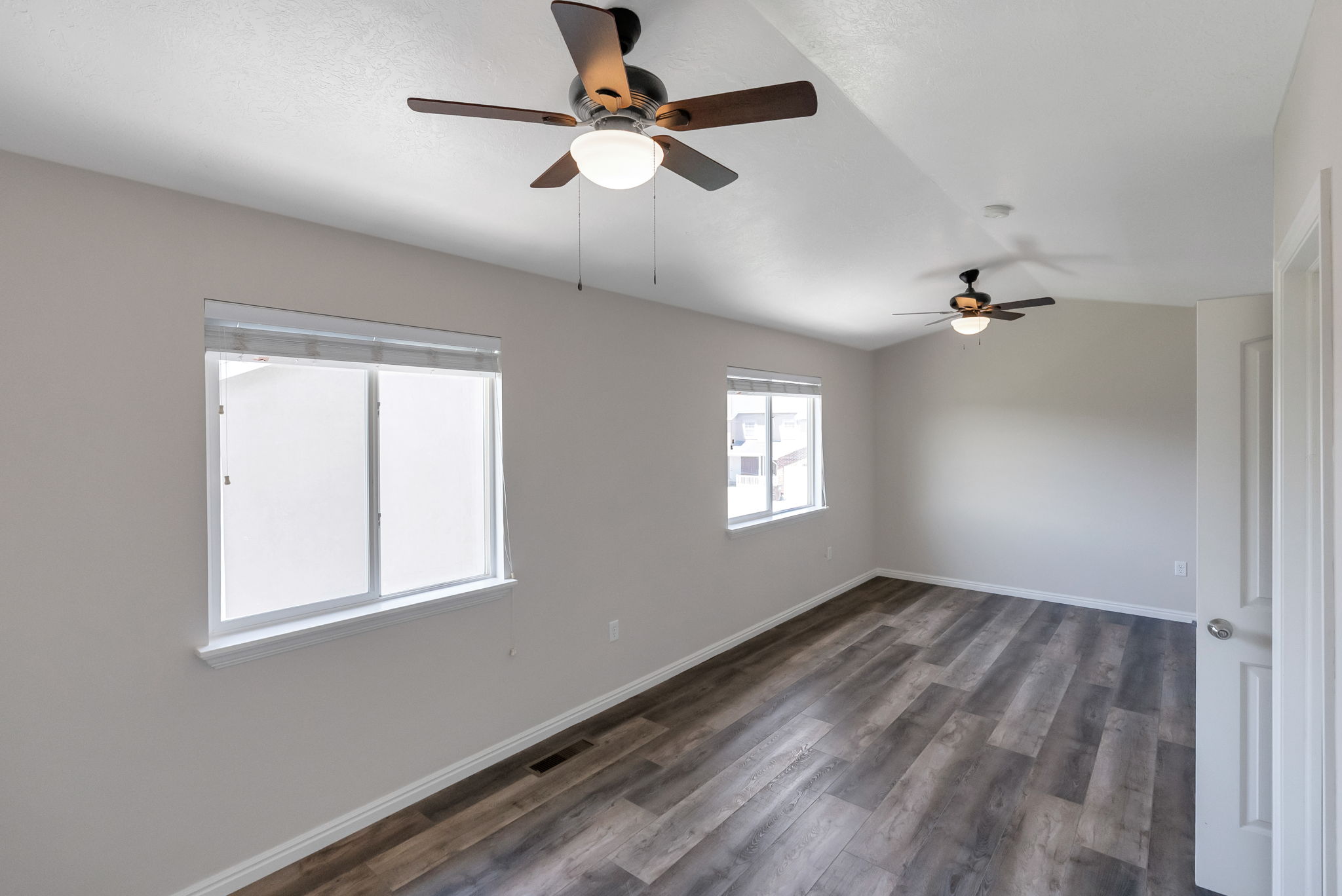 Spacious room featuring wood-finish flooring, light grey wall paint, and two windows