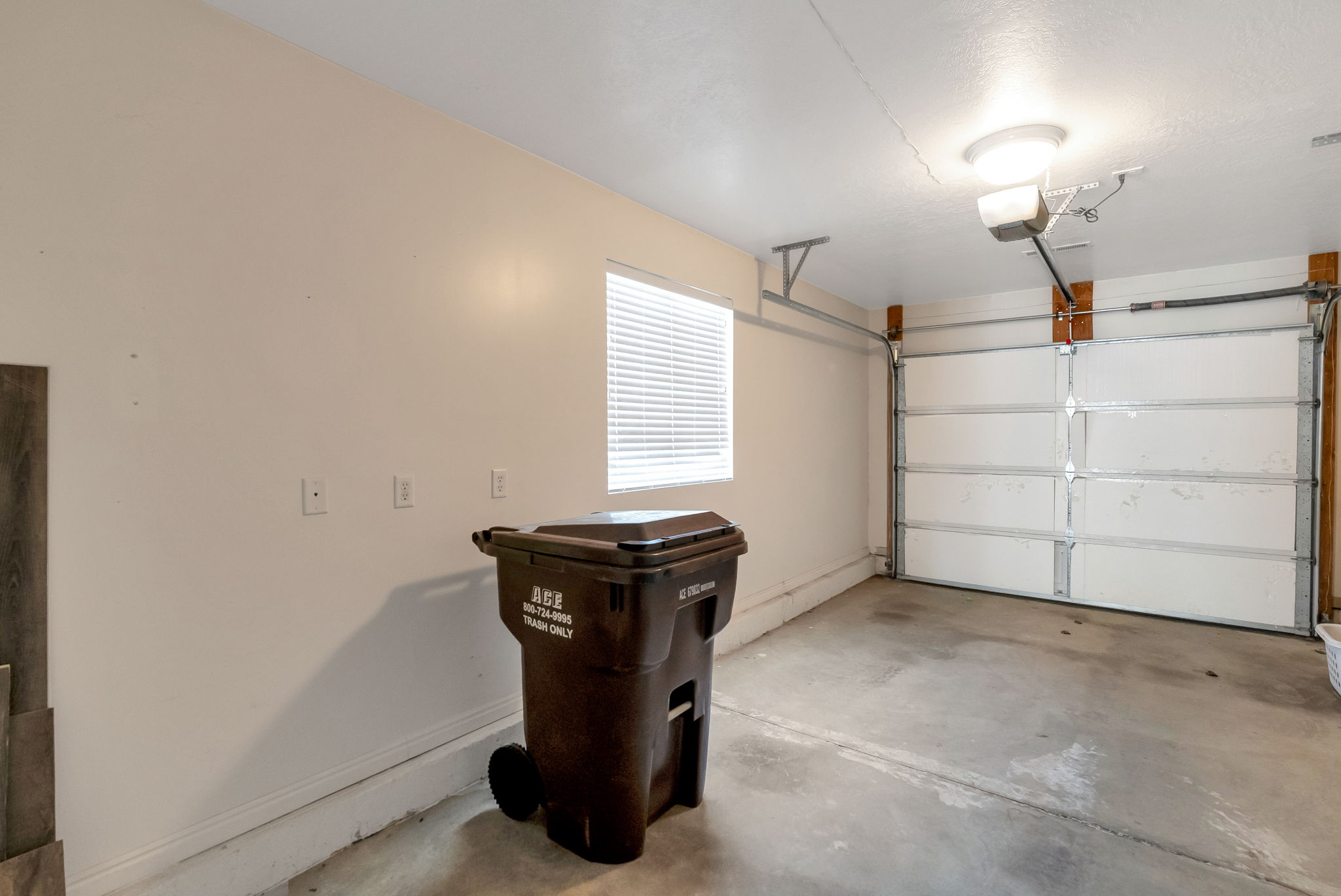 Single-car garage with concrete flooring, a window with blinds, and a white overhead garage door