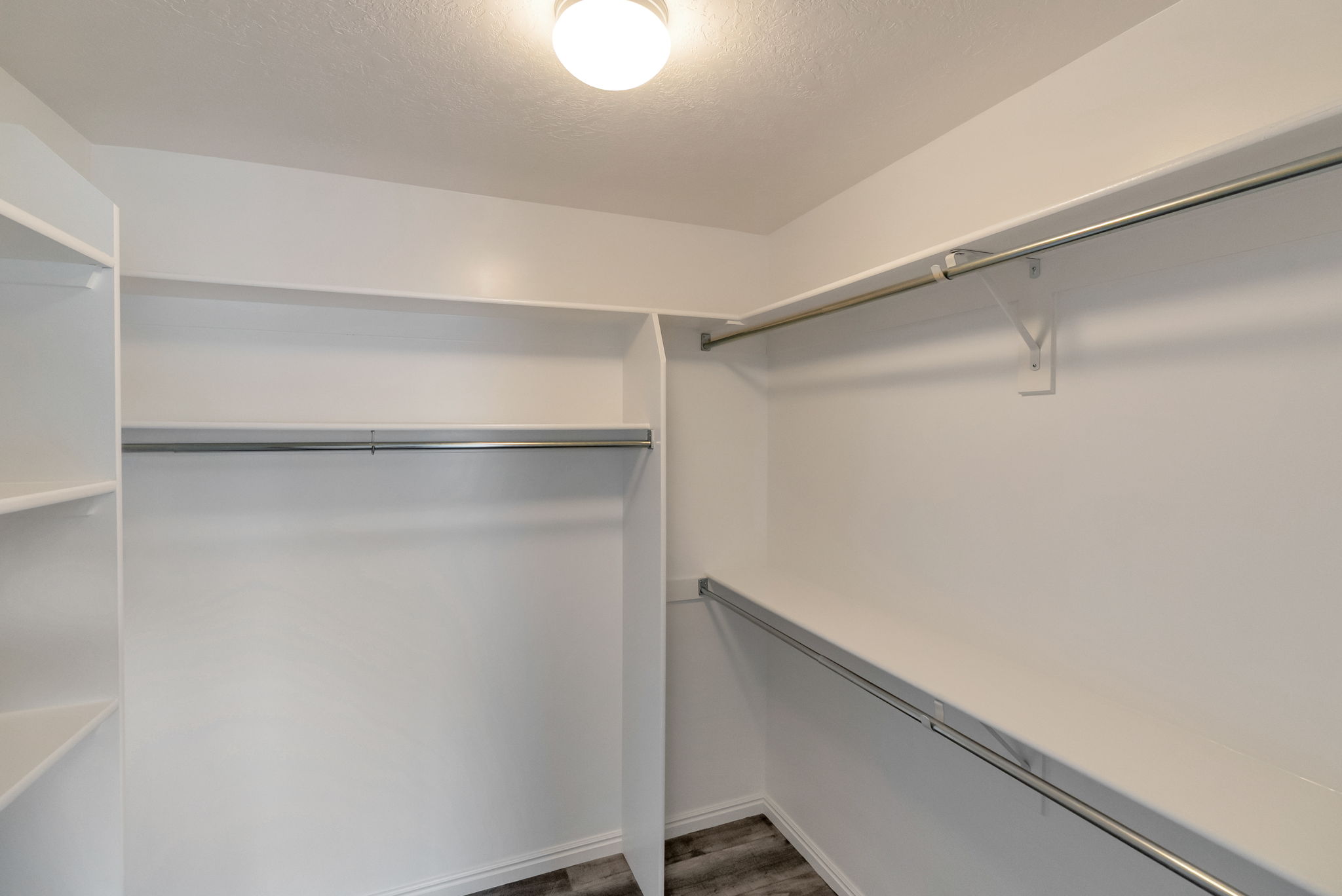 Walk-in closet featuring white walls, integrated shelving, and multiple metal hanging rods