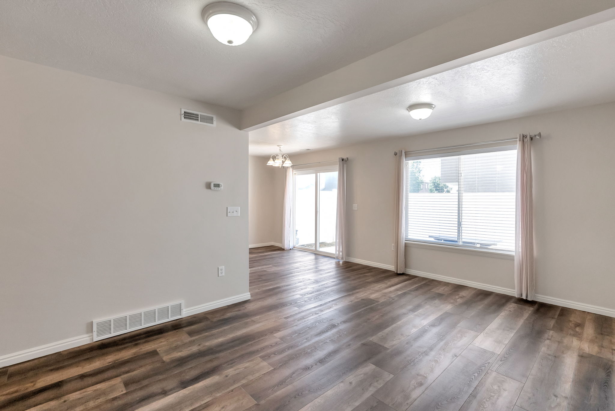 Spacious room featuring wood-finish flooring, a large window with blinds, and white trim