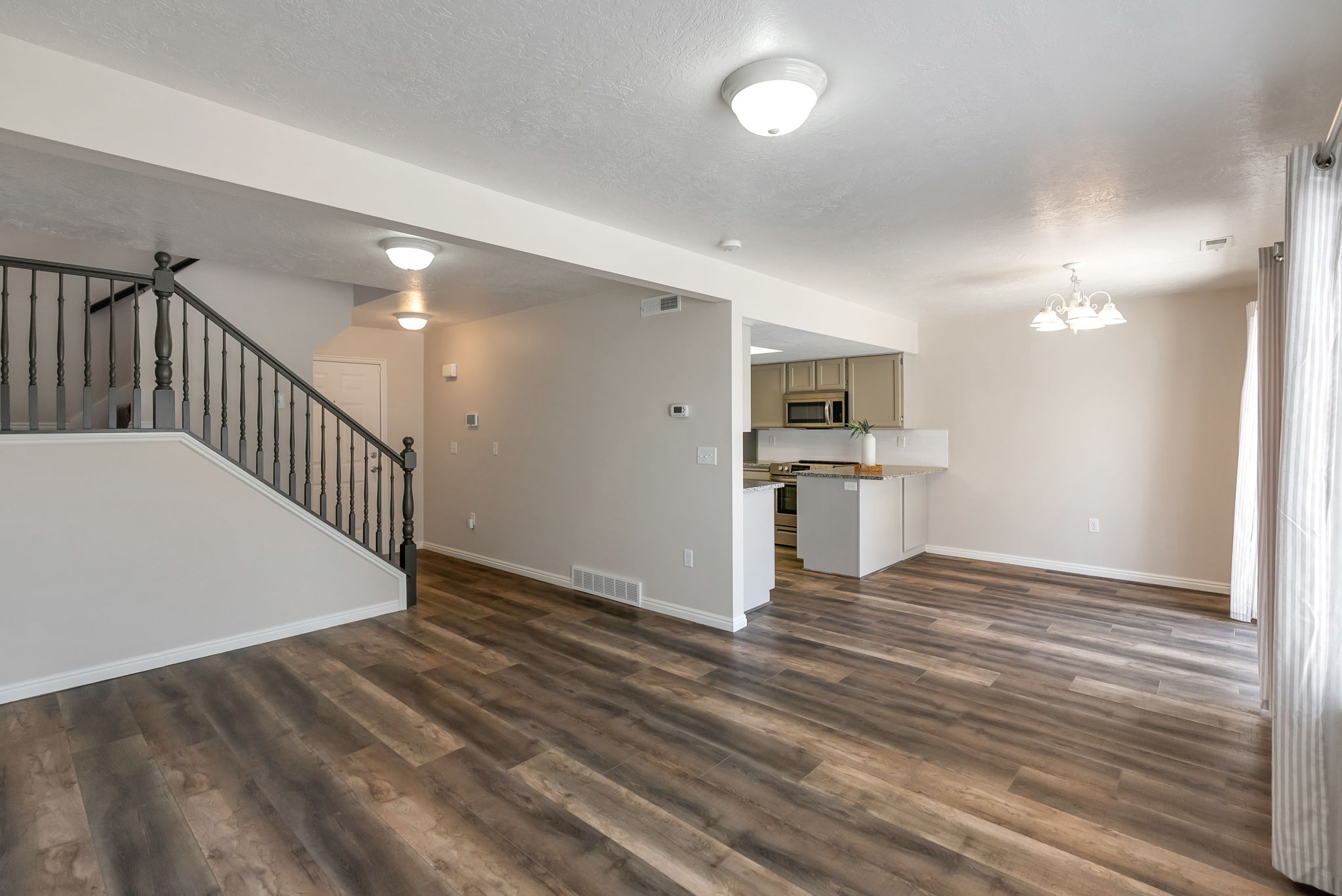 Open-concept living area featuring wood-finish flooring, a contemporary staircase with dark wood newel posts and balusters, and recessed ceiling lighting