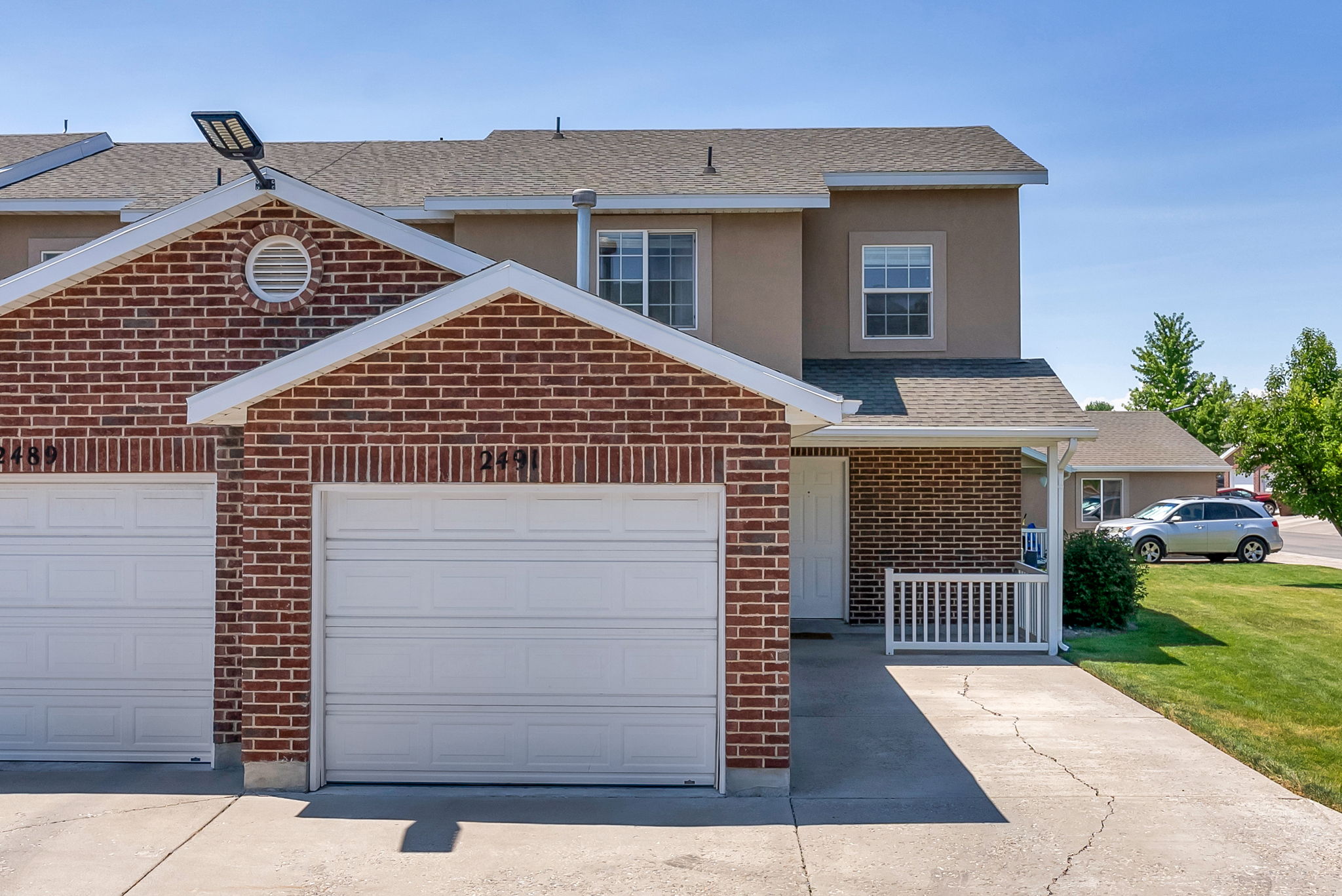 Brick and stucco exterior featuring a covered porch with white railing, attached garage, and a concrete driveway
