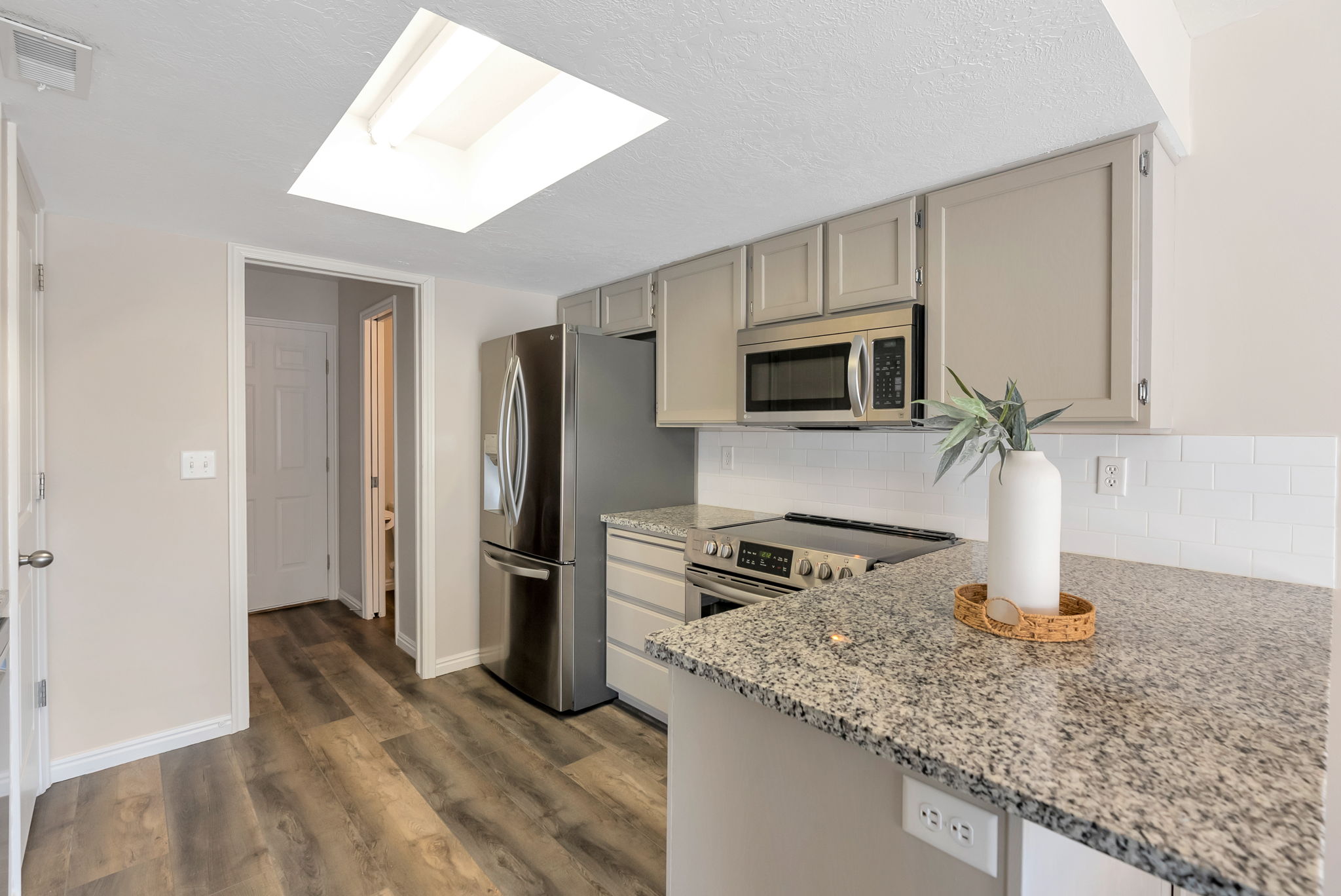 Kitchen featuring a skylight, wood-finish flooring, light gray cabinetry, stainless steel appliances, and speckled countertops