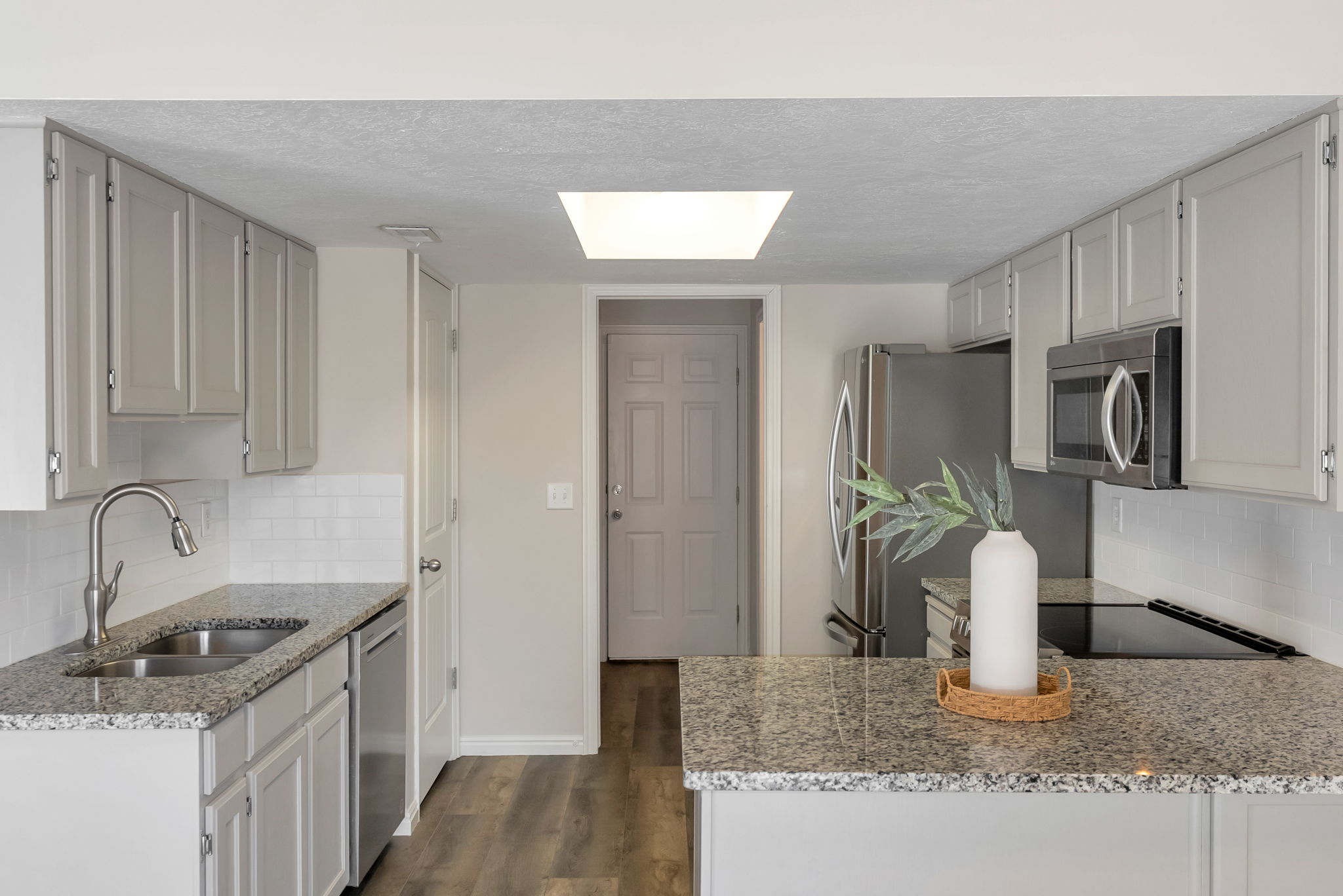 Kitchen featuring light grey cabinetry, granite-finish countertops, stainless steel appliances, a subway tile backsplash, and wood-finish flooring