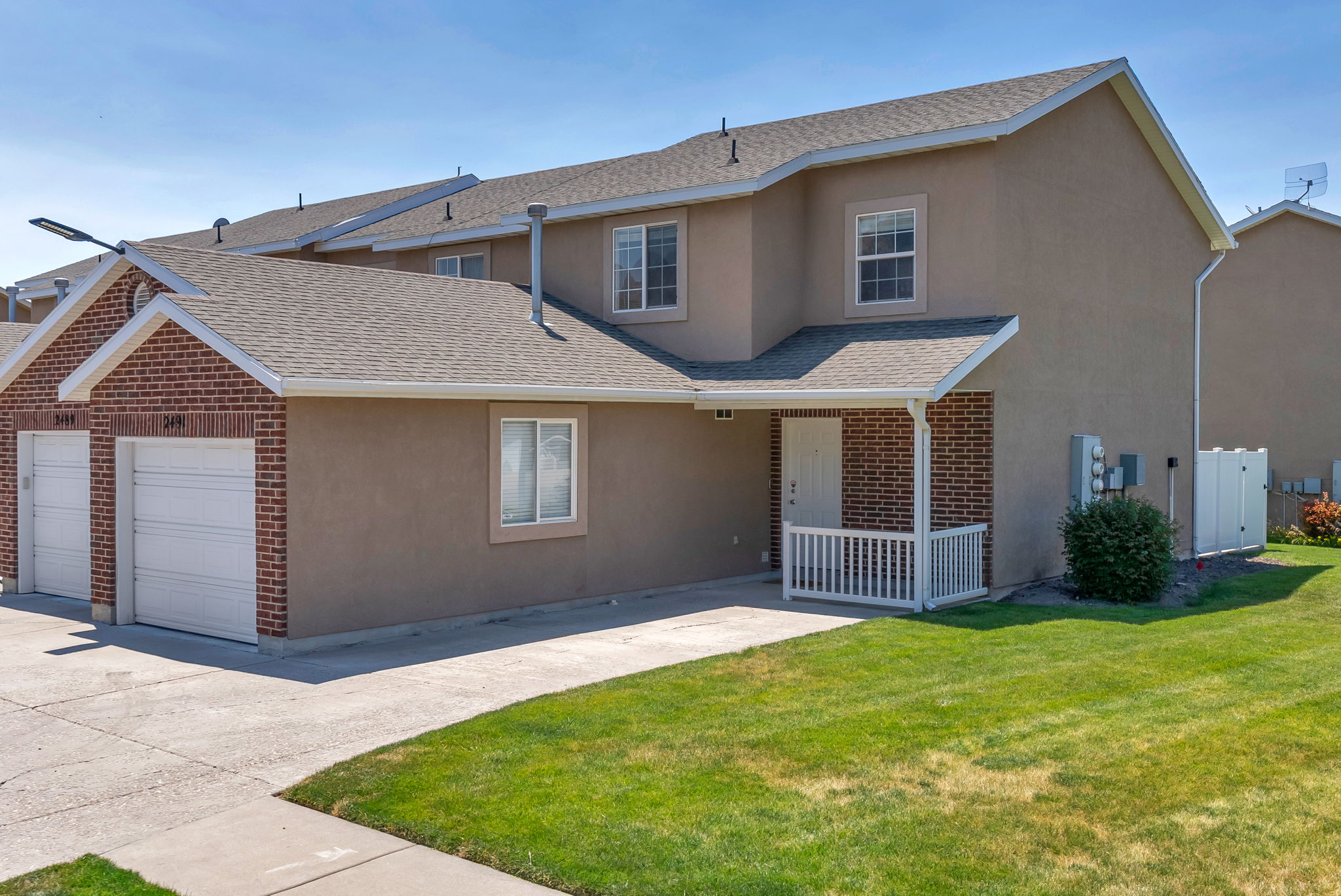 Stucco exterior with brick accents, featuring an attached garage with white doors, a covered porch with white railing, and a neatly manicured lawn
