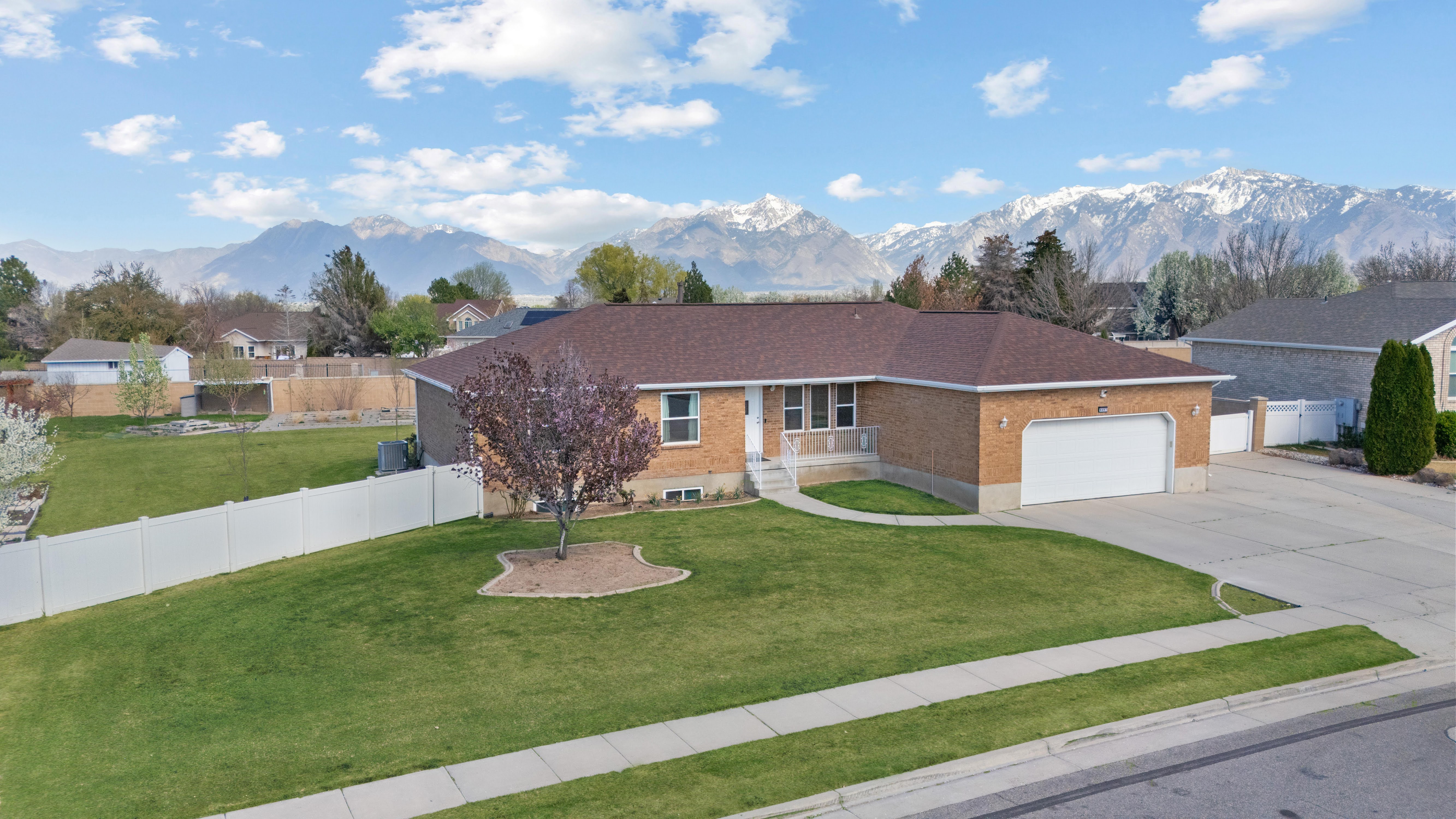 Brick exterior residence with a two-car garage, established front lawn, concrete driveway, and a white fence enclosing the property