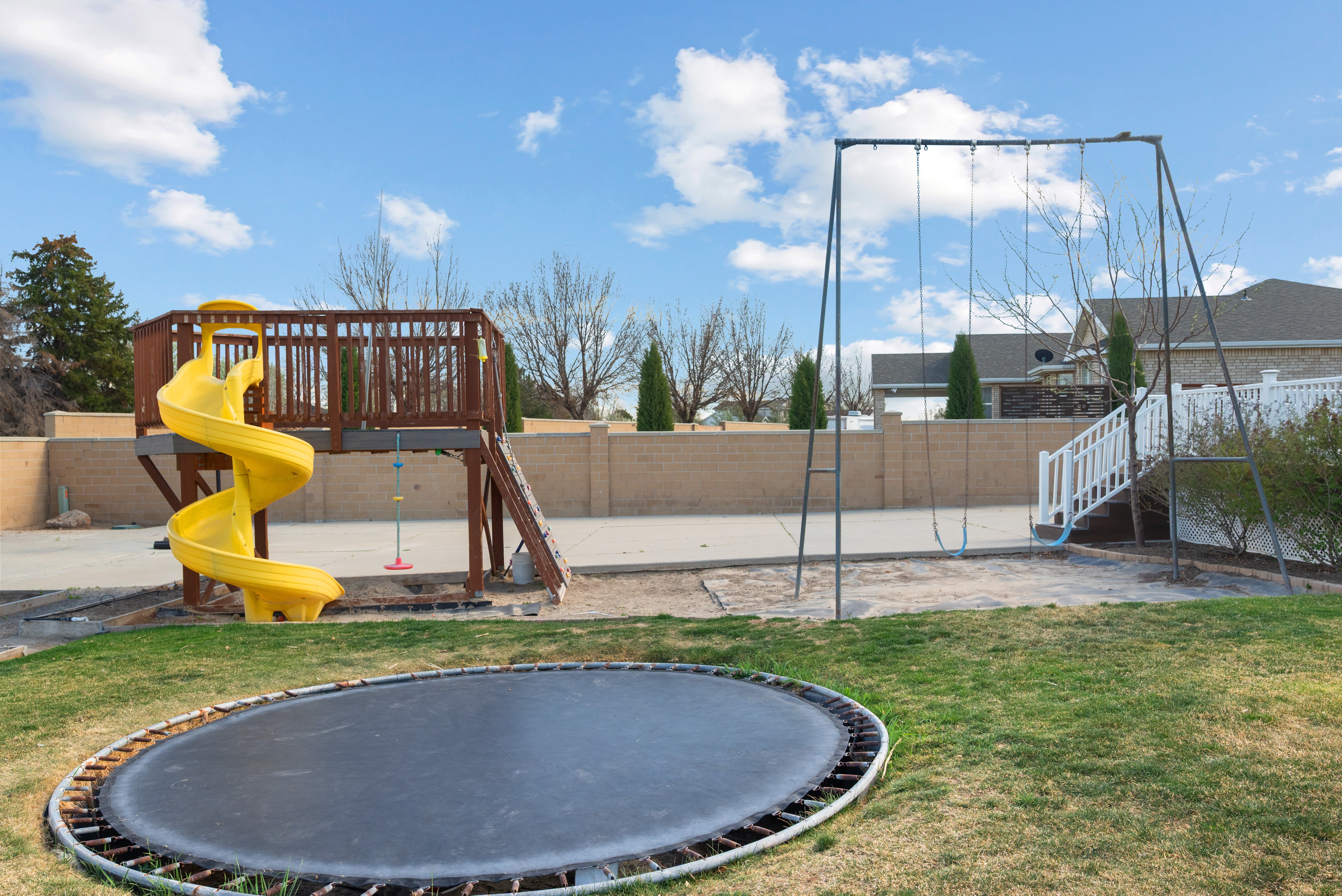 Expansive backyard featuring a built-in trampoline, wooden playset with a spiral yellow slide, and a swing set