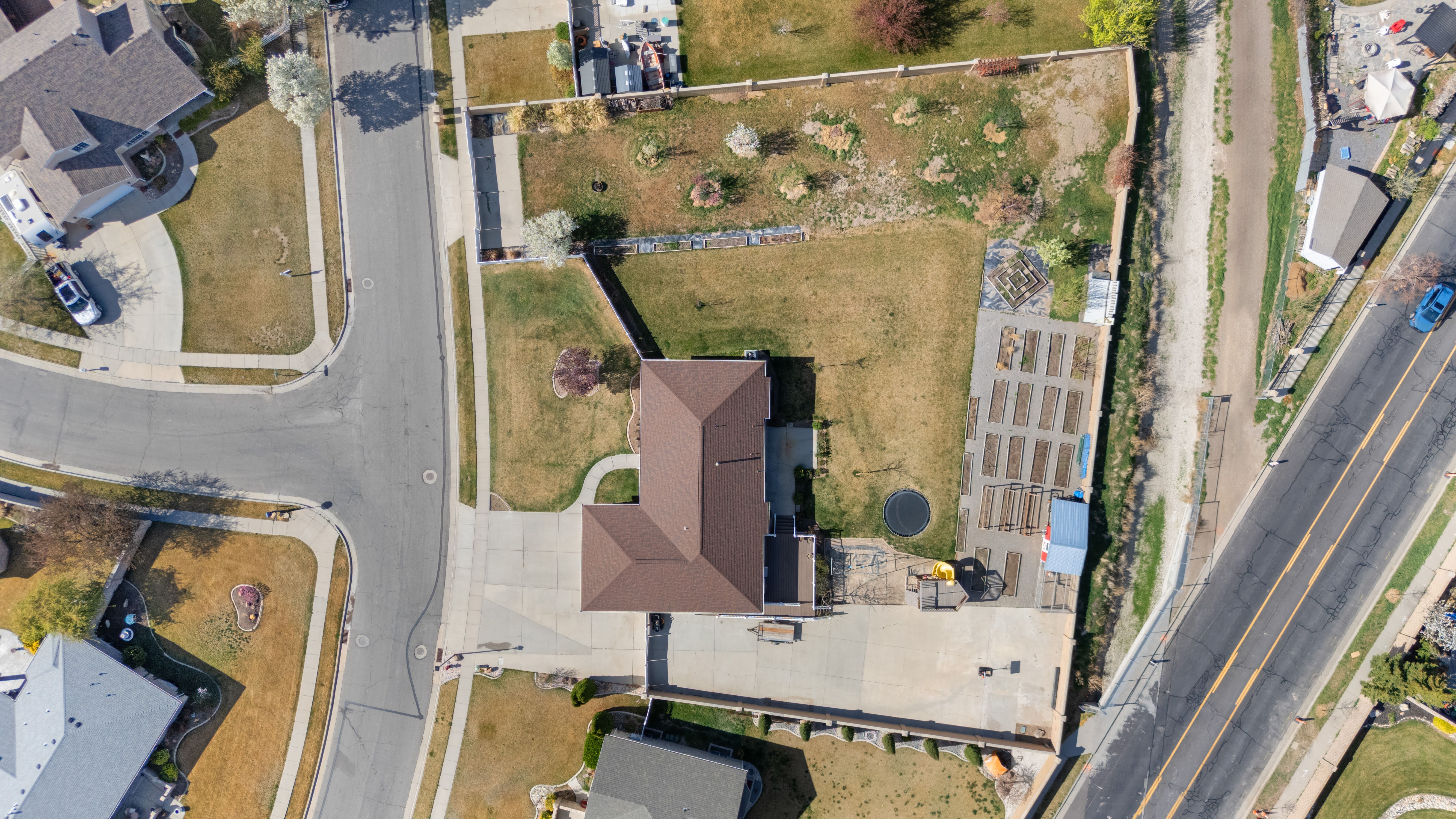 Expansive property featuring a brown roofline, a large paved driveway, a considerable grassy area, and a dedicated garden bed section